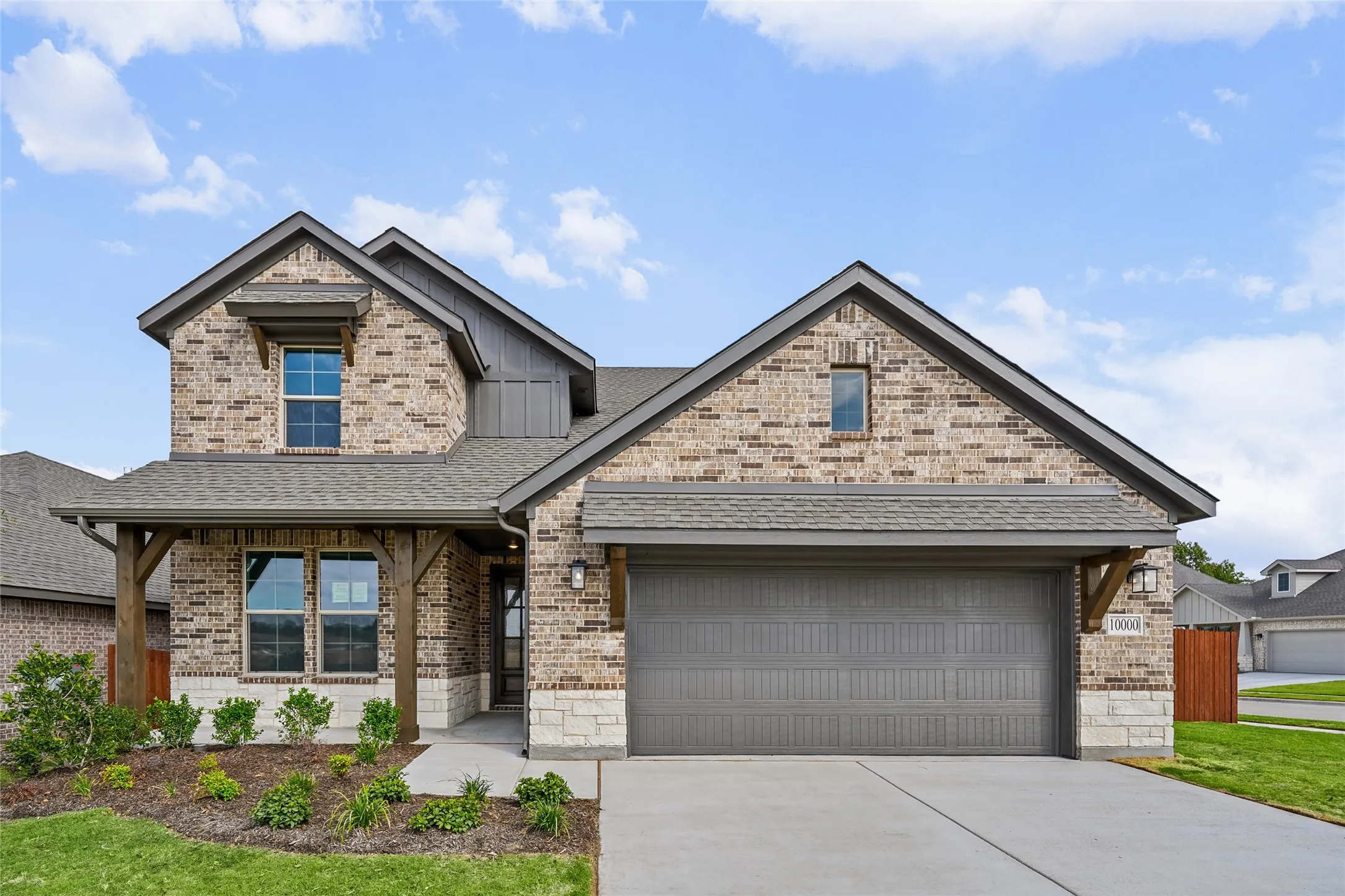 Brick and stone exterior with a covered entry, decorative wood columns, and an integrated two-car garage