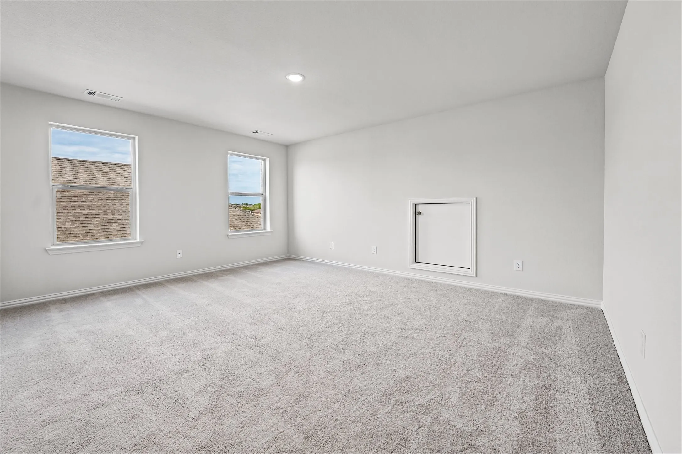 Spacious room with light-toned carpeting, dual windows, recessed lighting, and a white wall access panel