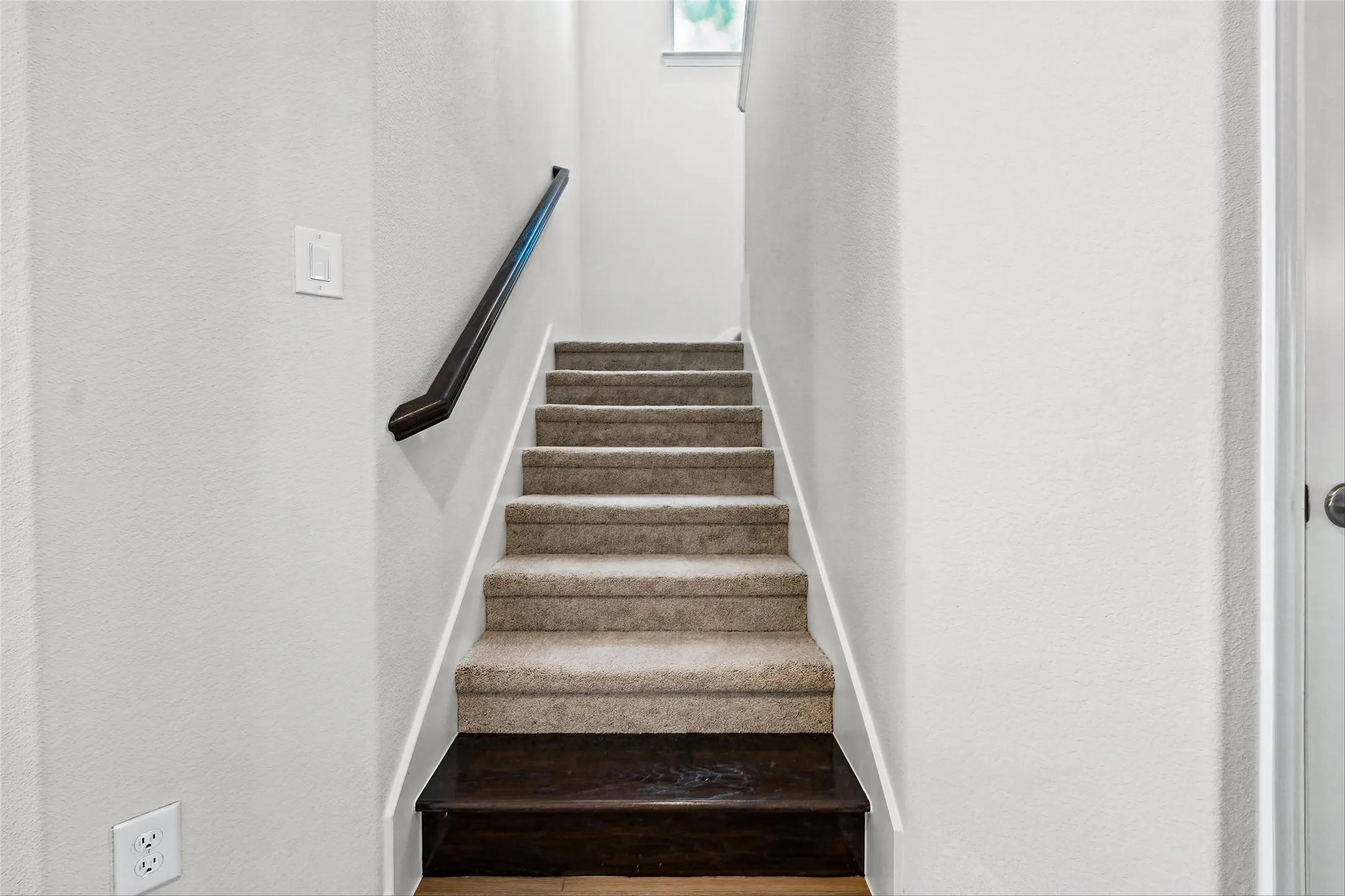 Staircase featuring carpeted treads, a dark wood-finish landing, and a dark handrail