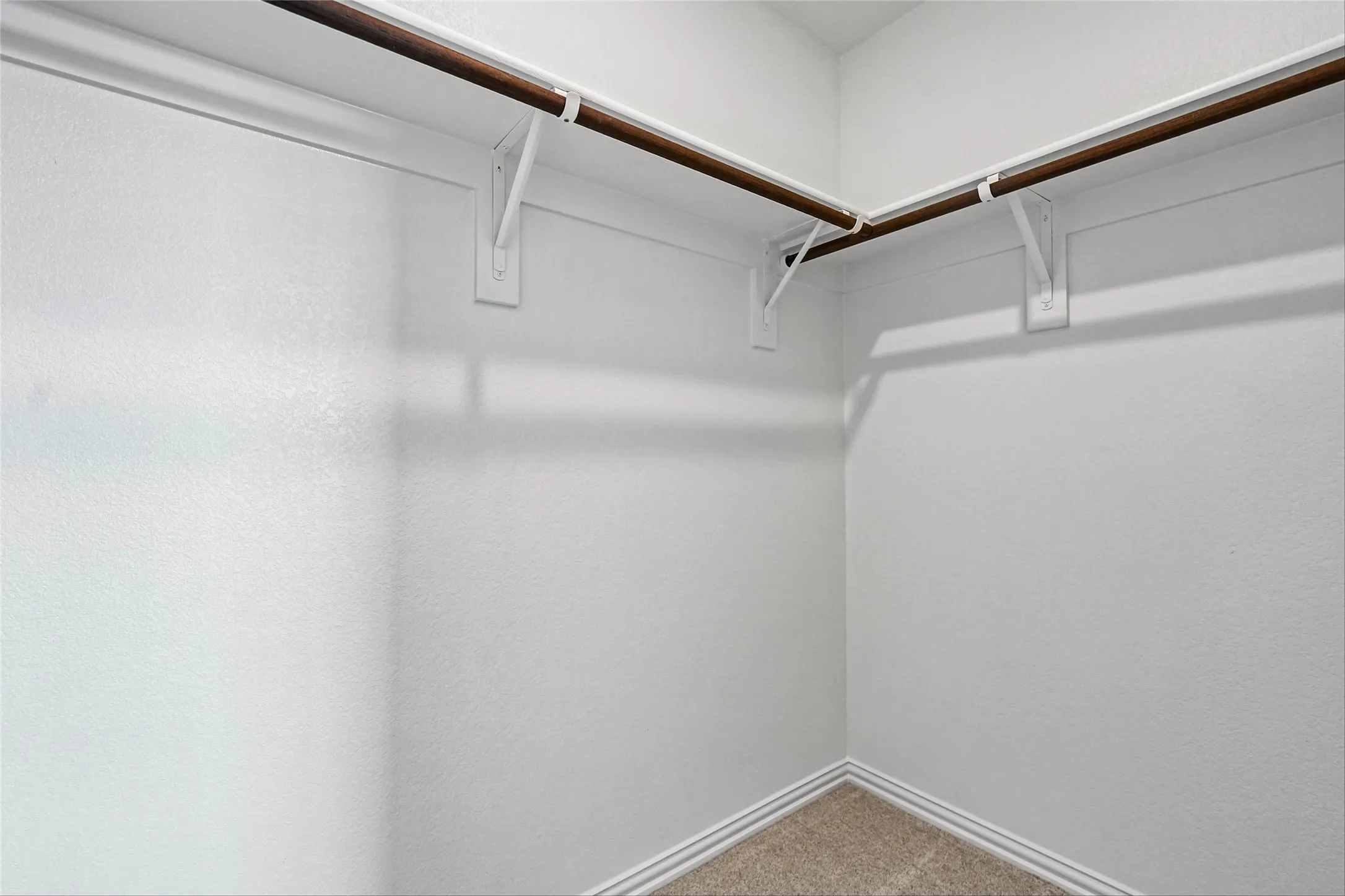 Corner closet with white walls, L-shaped hanging rod, and light brown carpeting