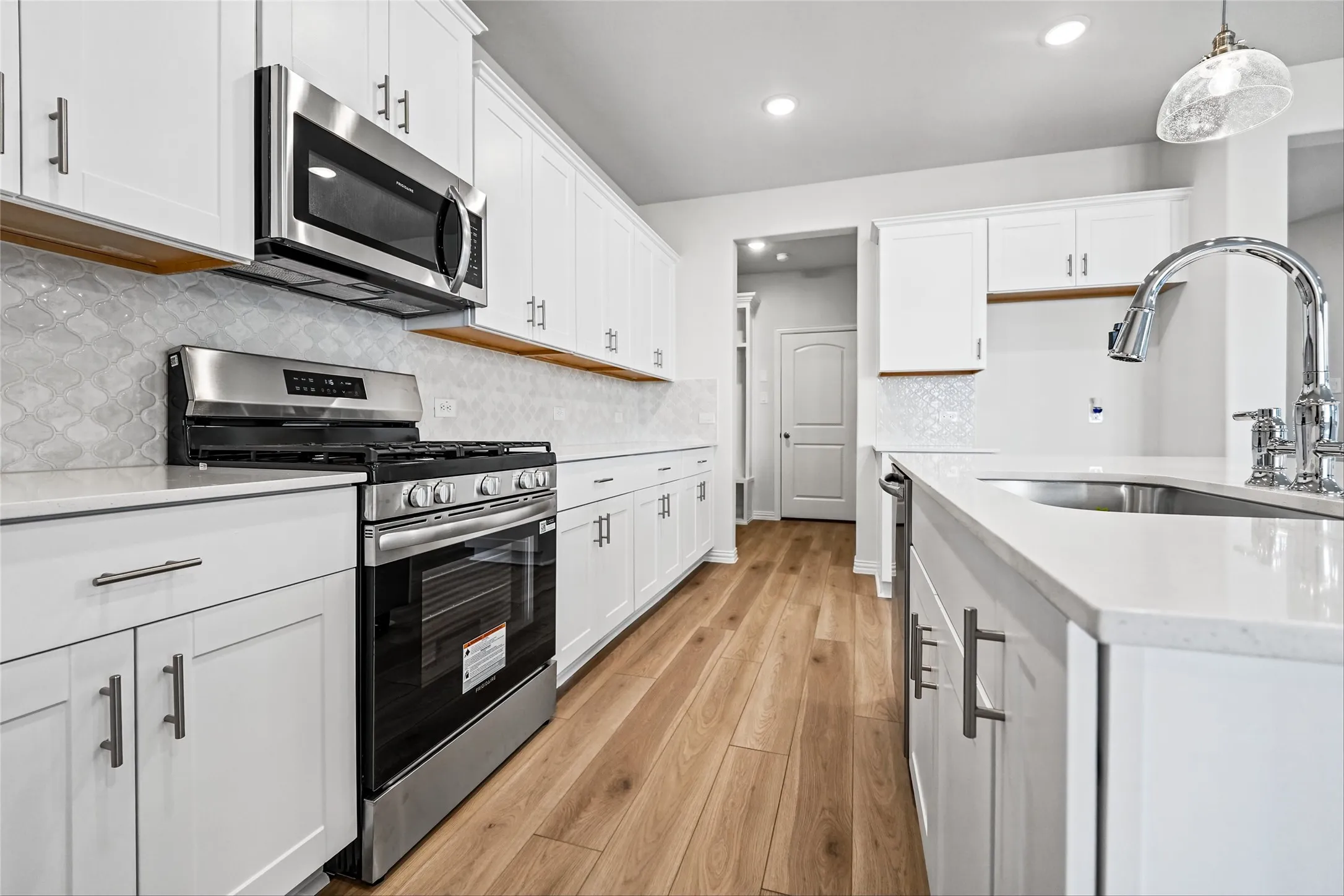 White cabinetry, stainless steel appliances, wood-finish flooring, white countertops, and a tile backsplash