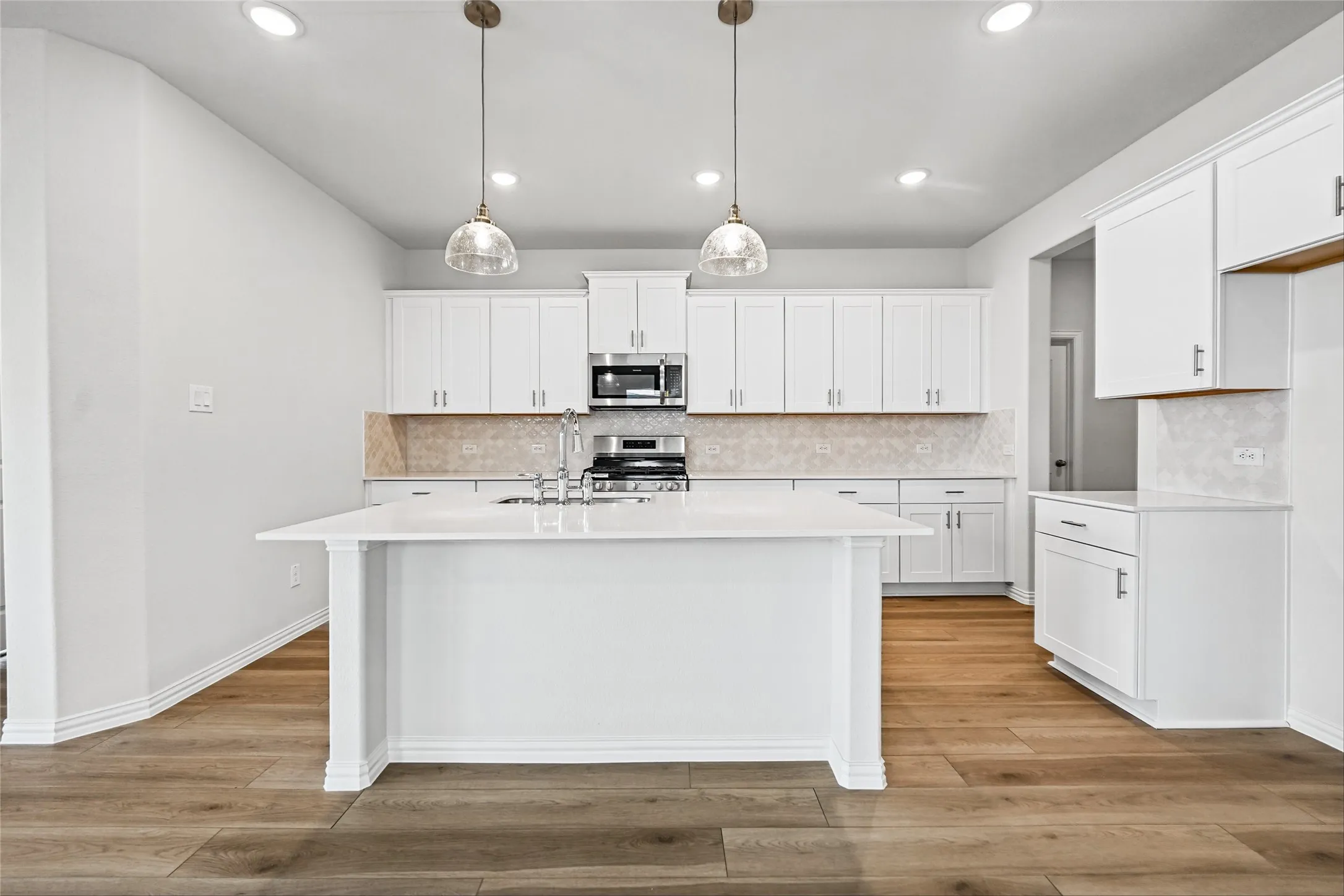 Kitchen featuring white cabinetry, a central island with a sink, stainless steel appliances, a tile backsplash, and wood-finish flooring