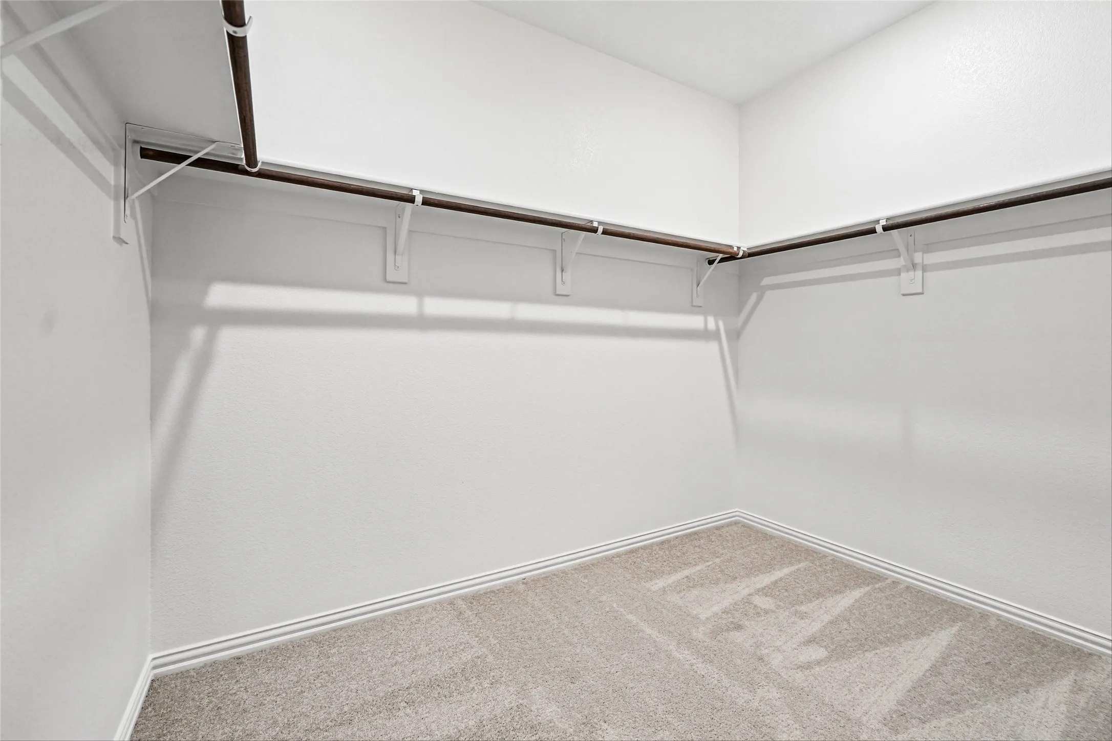 L-shaped hanging rods with white shelving brackets, light neutral carpet, and white walls
