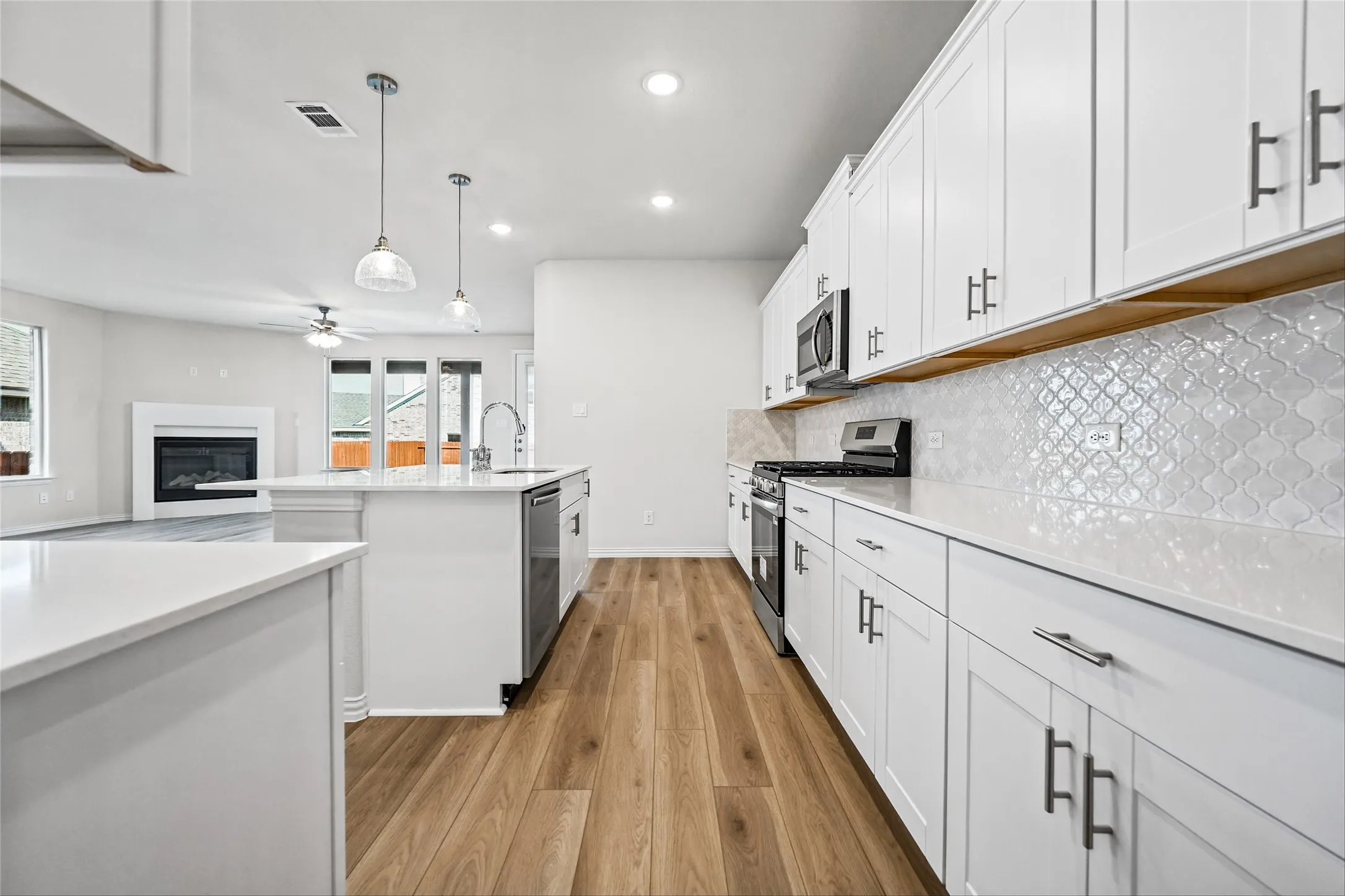 Contemporary kitchen featuring white cabinetry, light-toned countertops, a geometric tile backsplash, and wood-finish flooring