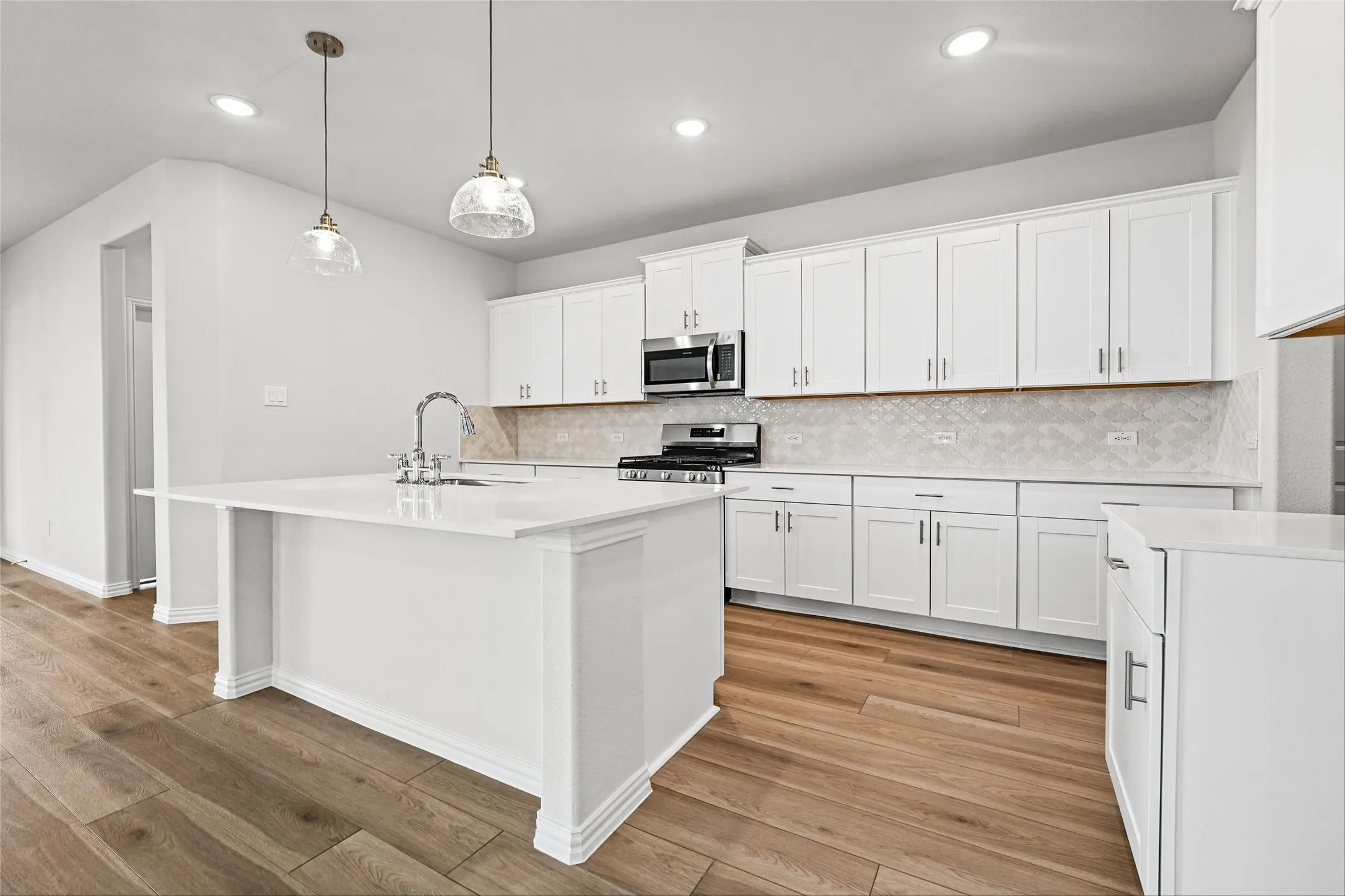 Gourmet kitchen featuring a central island with a sink, white cabinetry, integrated stainless steel appliances, a tile backsplash, and wood-finish flooring