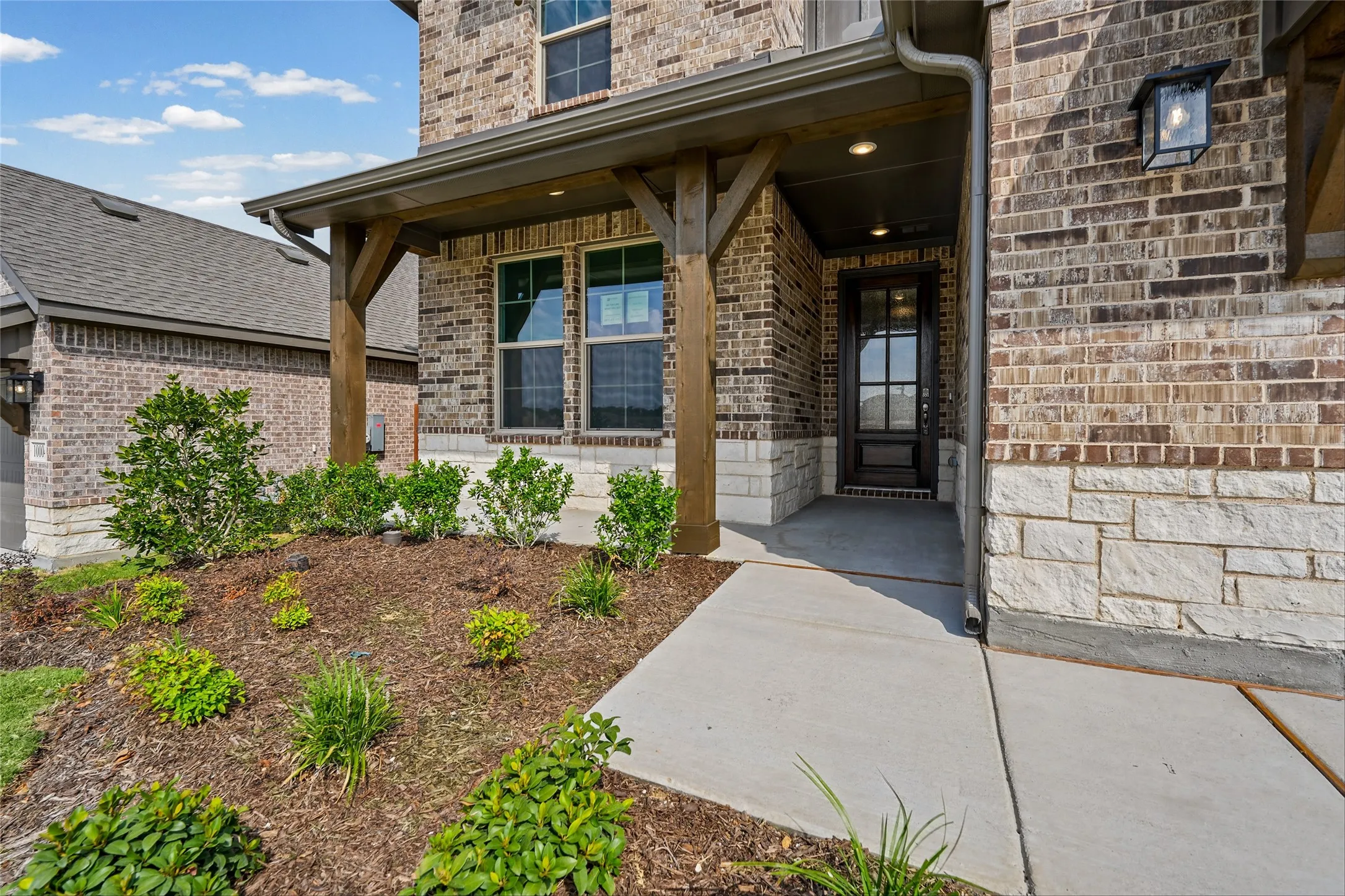 Brick and stone exterior featuring a covered entry, wood-finish columns, and a paneled front door with glass inserts