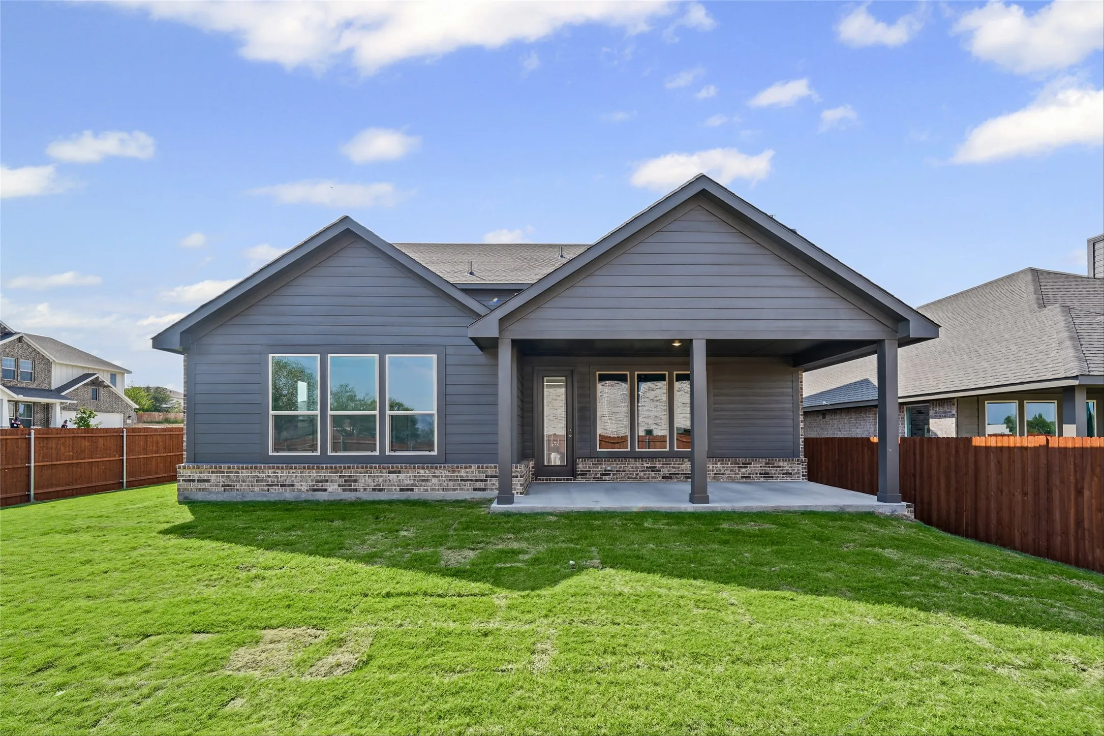 Exterior featuring a covered patio, dark gray siding, a shingled roof, a partial brick facade, and multiple windows