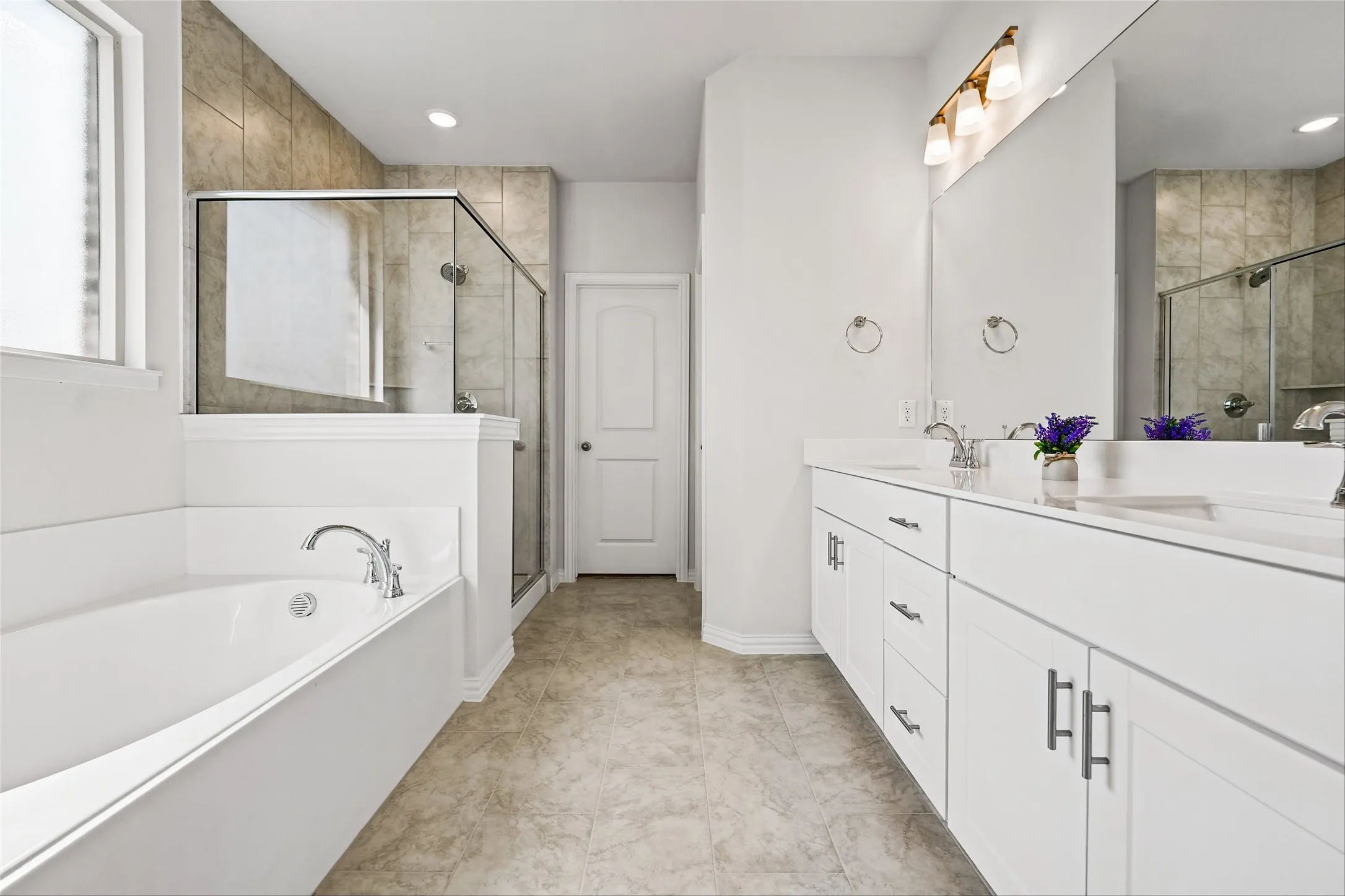 Dual vanity with white cabinetry, built-in bathtub, glass-enclosed shower, and tiled flooring