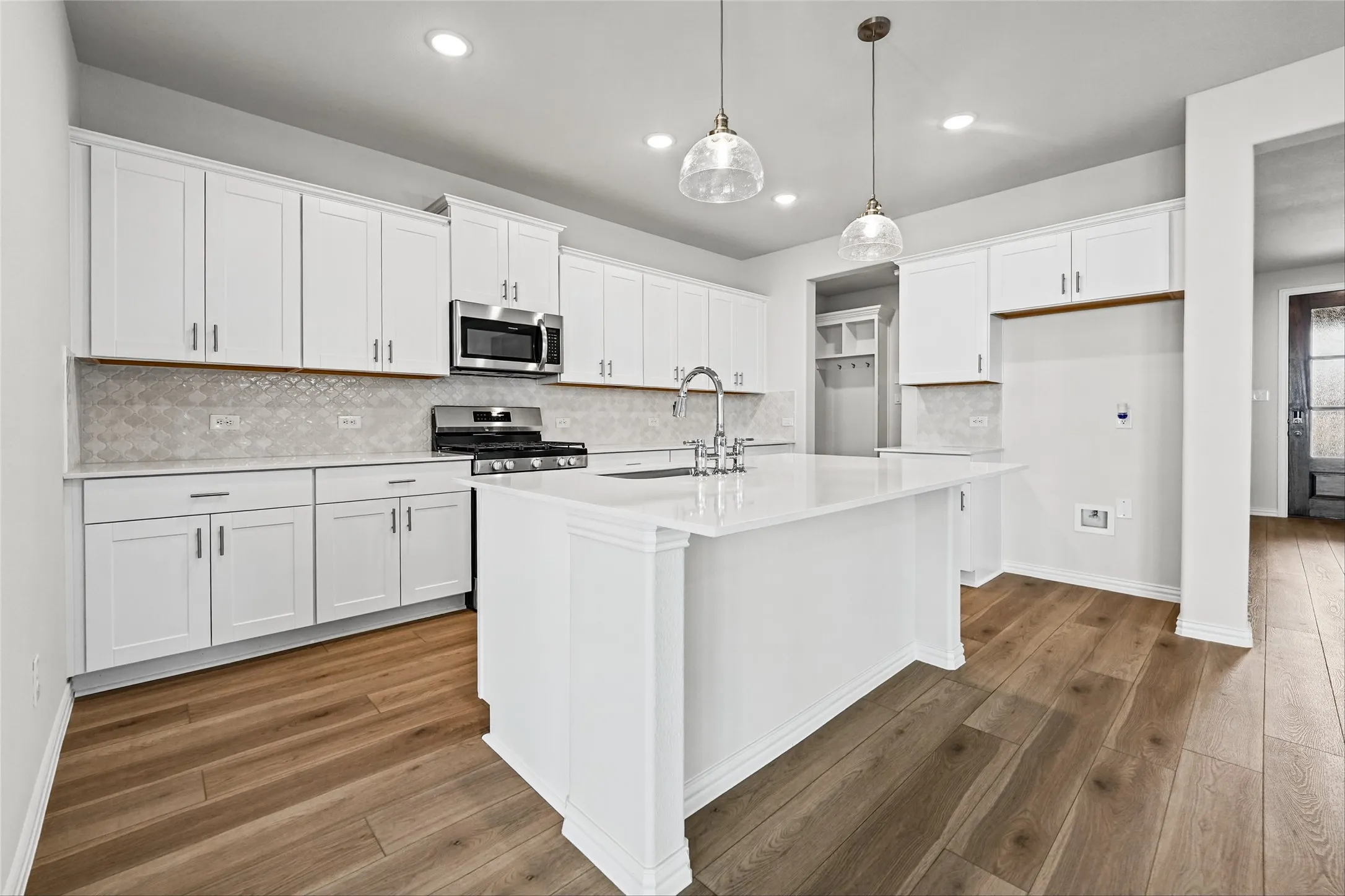 Modern kitchen featuring white cabinetry, a central island with a sink, stainless steel appliances, and wood-finish flooring