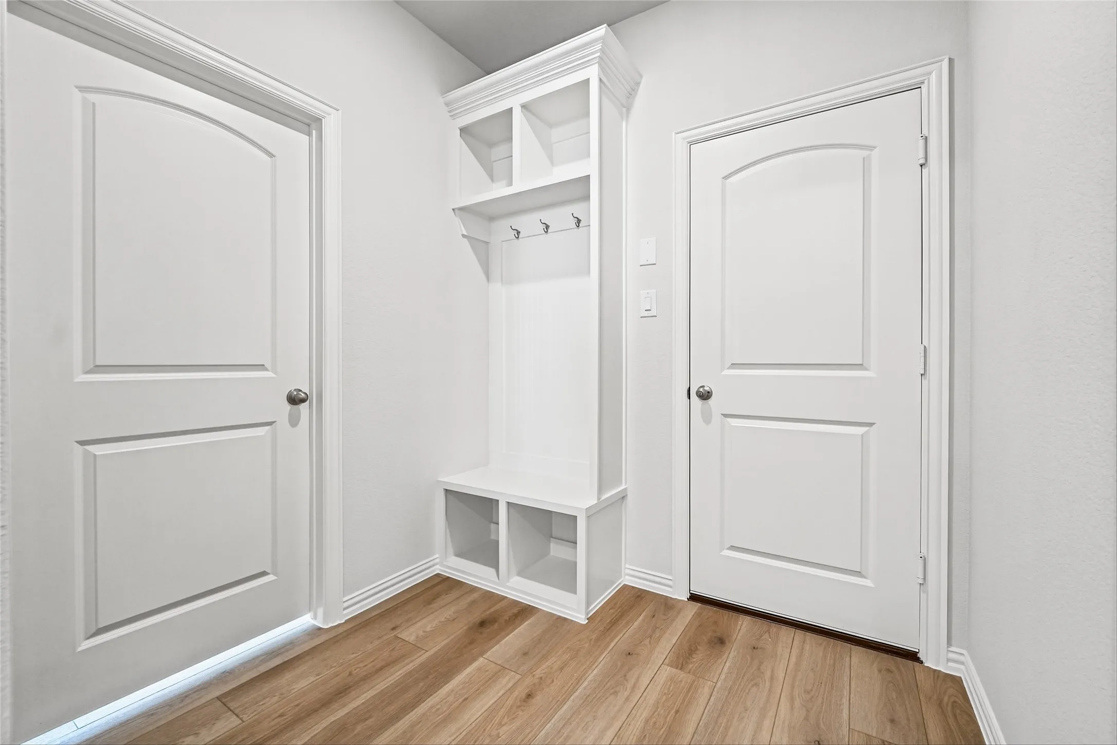 Built-in white mudroom bench with storage cubbies and upper shelving, featuring integrated coat hooks and wood-finish flooring