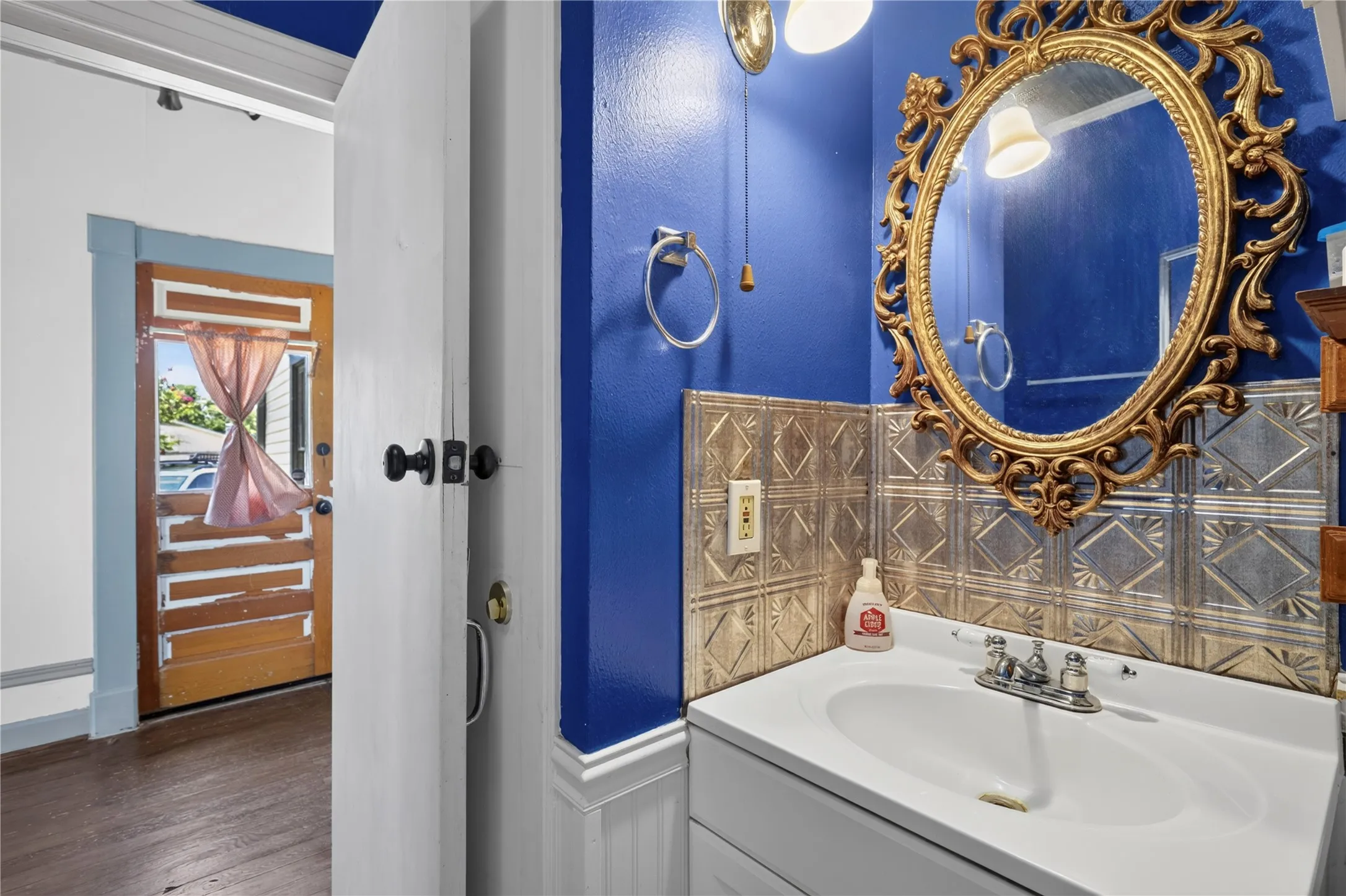 Bathroom vanity with a white basin sink and chrome faucet, set against a blue wall with decorative metal tile wainscoting