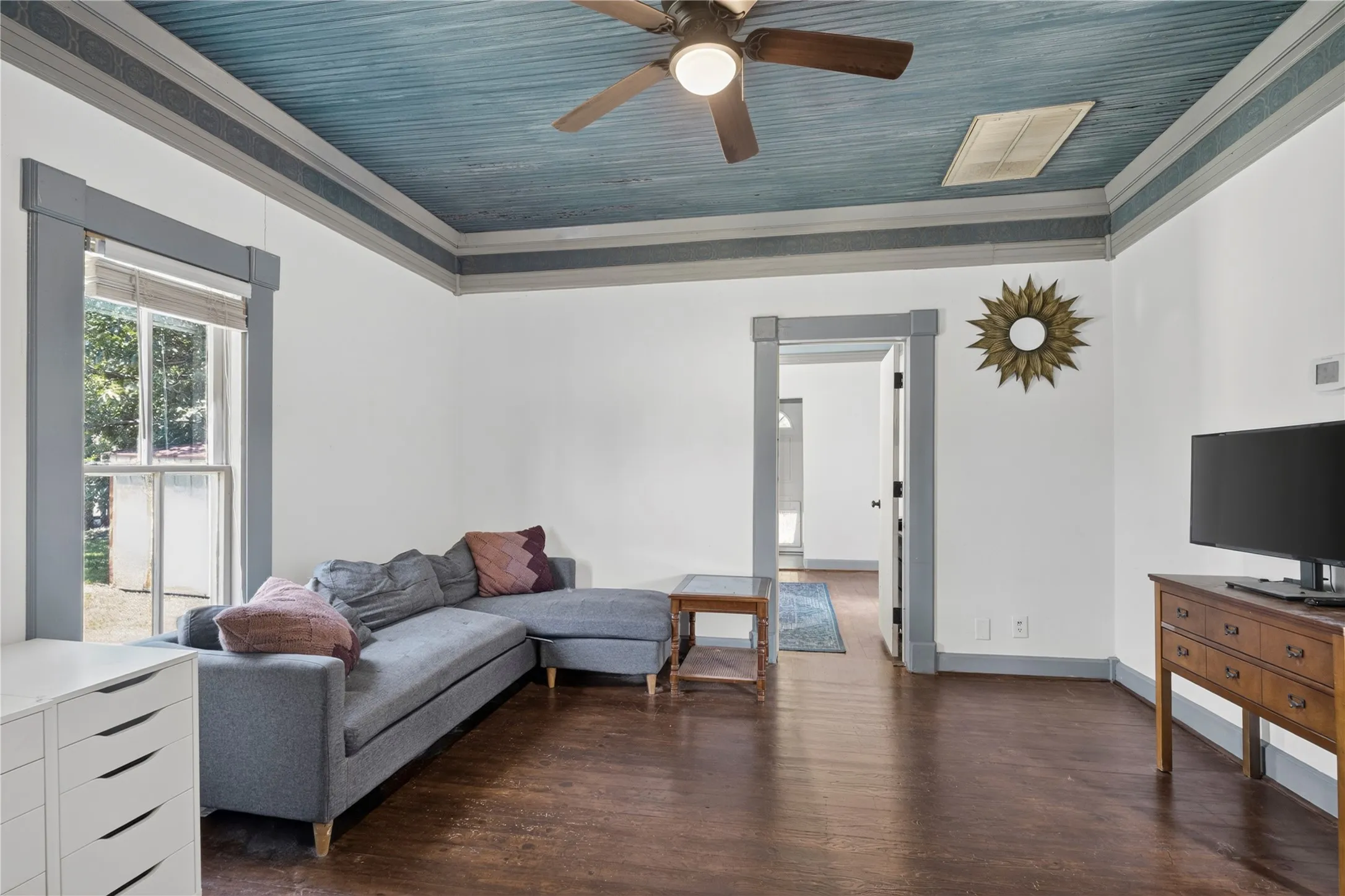 Living area featuring dark wood-finish flooring, white walls, and a blue wood ceiling with a ceiling fan