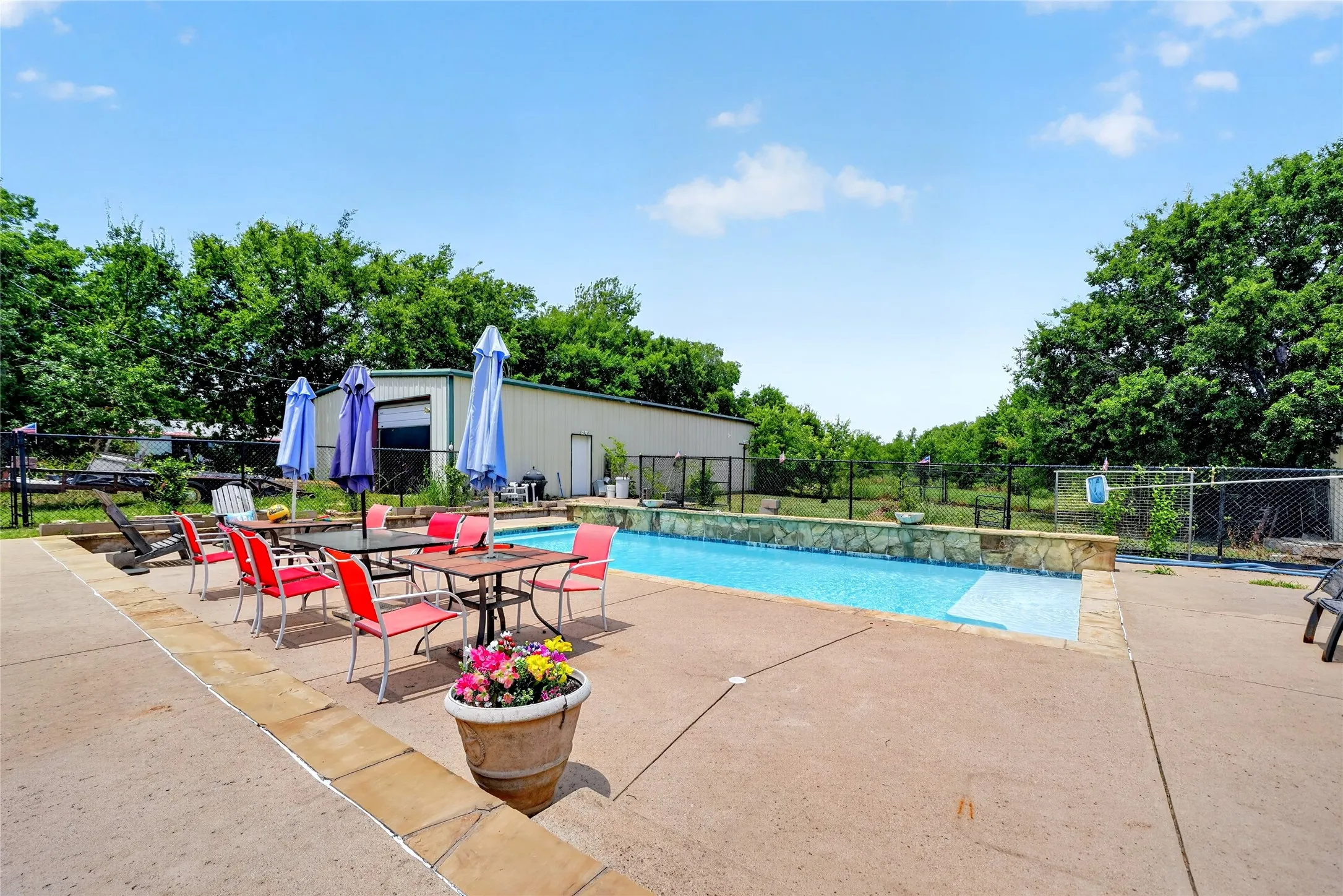 Outdoor swimming pool with integrated spa, bordered by a stone wall and expansive concrete decking