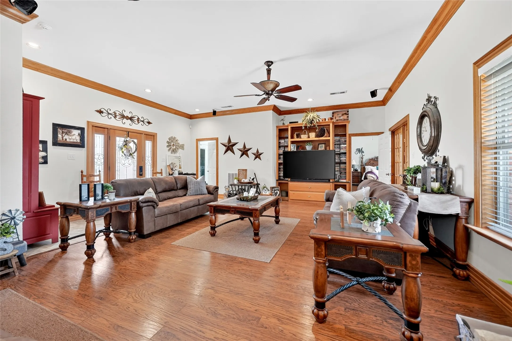 Spacious living area featuring wood-finish flooring, a ceiling fan, recessed lighting, crown molding, and a built-in entertainment center with shelving