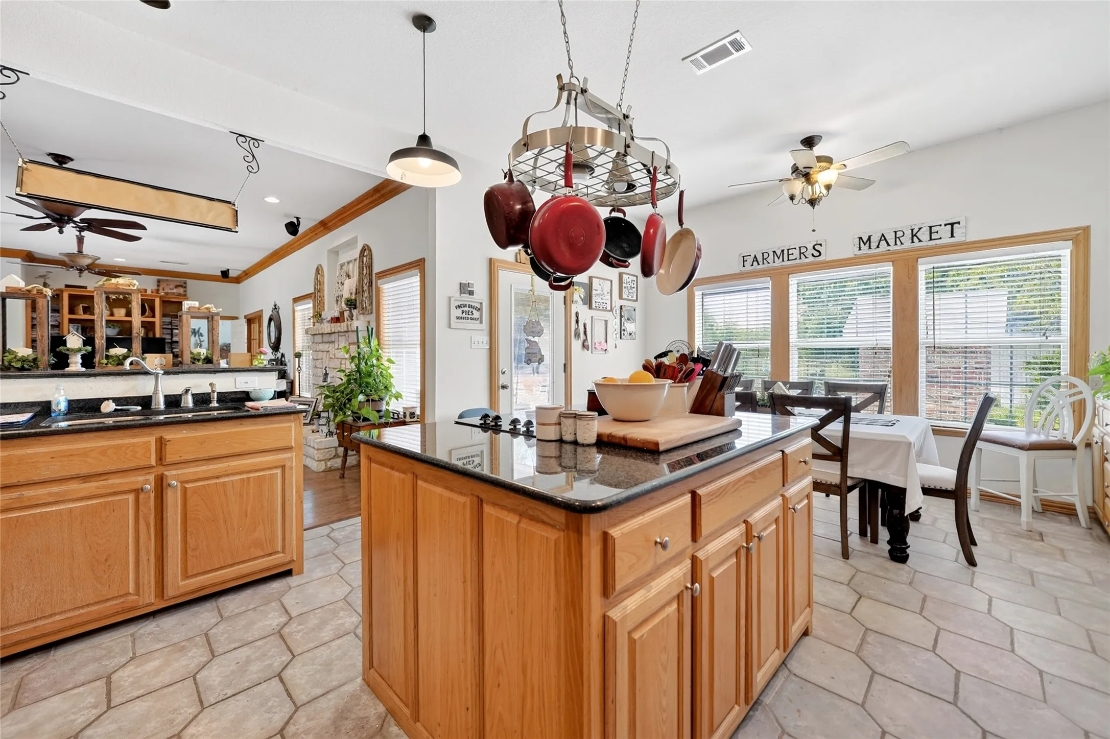 Kitchen featuring a central island with a dark countertop and light wood cabinetry, stone-look tile flooring, and a dining area with multiple windows