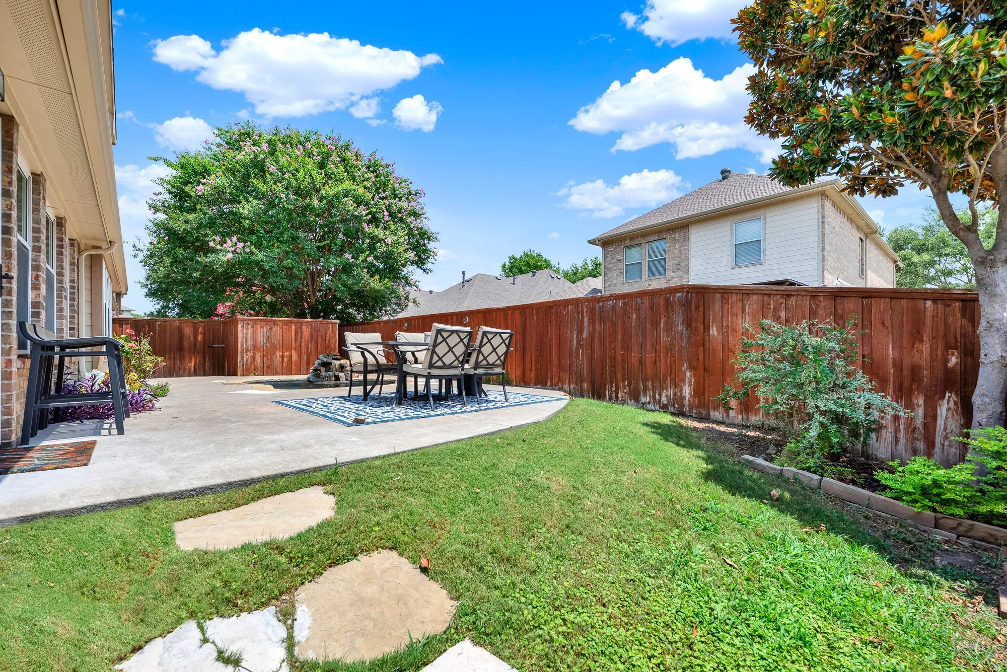 The generous patio flows into a grassy yard with room for pets, play, or gardening, all framed by mature landscaping and shade trees. Imagine hosting summer cookouts while kids or dogs still have space to run and enjoy the outdoors.