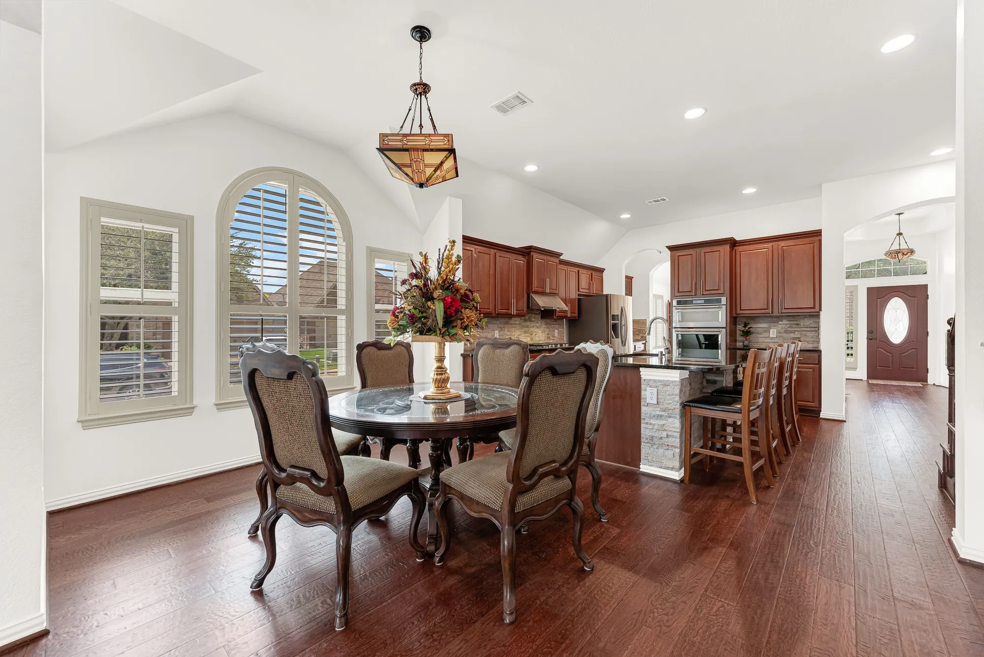 Natural light pours through the elegant arched window, highlighting the soaring ceiling and rich wood flooring while creating a seamless connection to the kitchen. Gather around the table for holiday dinners, weekend brunches, or relaxed evenings where everyone stays connected.