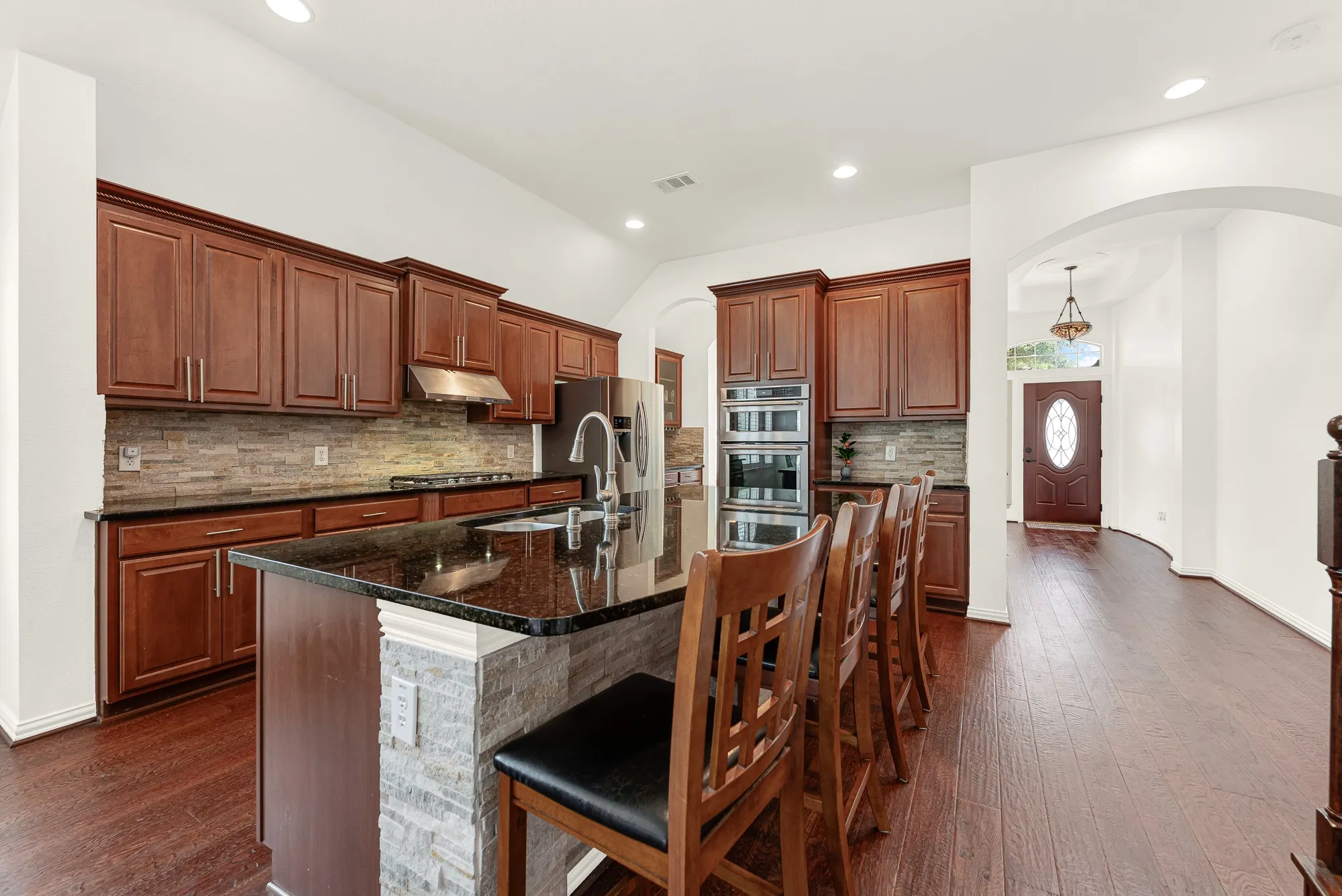 The oversized granite island with extra seating anchors the kitchen, while rich wood flooring and soaring ceilings create a warm, open flow into the living and dining areas. It's the perfect place for casual meals, visiting with guests, or gathering while dinner is underway.