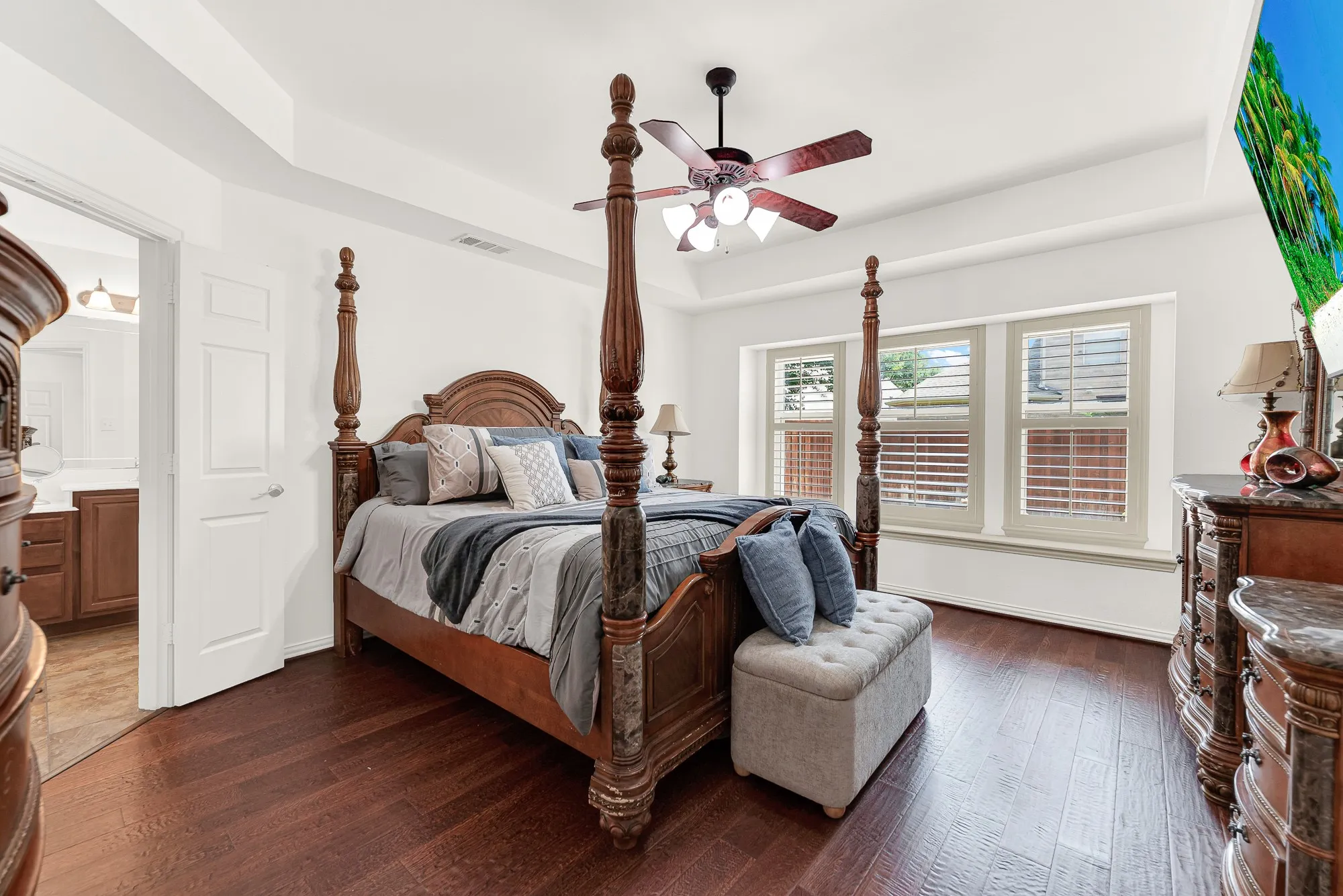 The spacious primary suite features rich wood flooring, a tray ceiling, and a wall of windows that fills the room with natural light. Start each morning in a peaceful retreat with plenty of space to unwind before the day begins.