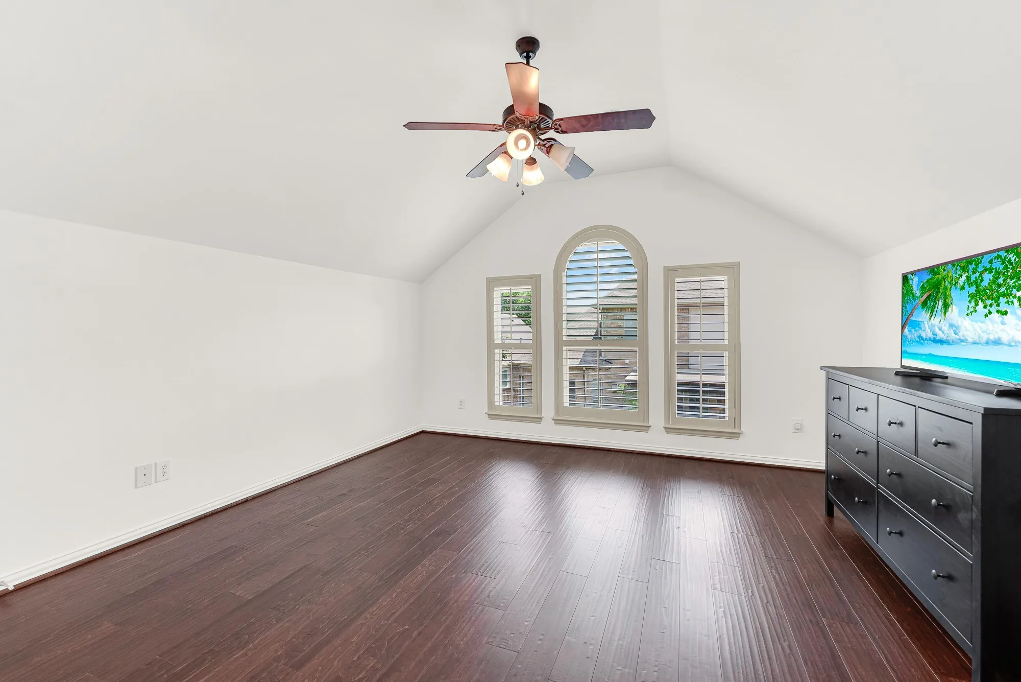 A spacious upstairs bedroom offers exceptional flexibility, featuring vaulted ceilings, rich hardwood flooring, a ceiling fan, and an oversized window arrangement that fills the room with natural light. With ample space for a king-sized bed, seating area, or home office, this private retreat is perfect for guests, teens, or multi-generational living.