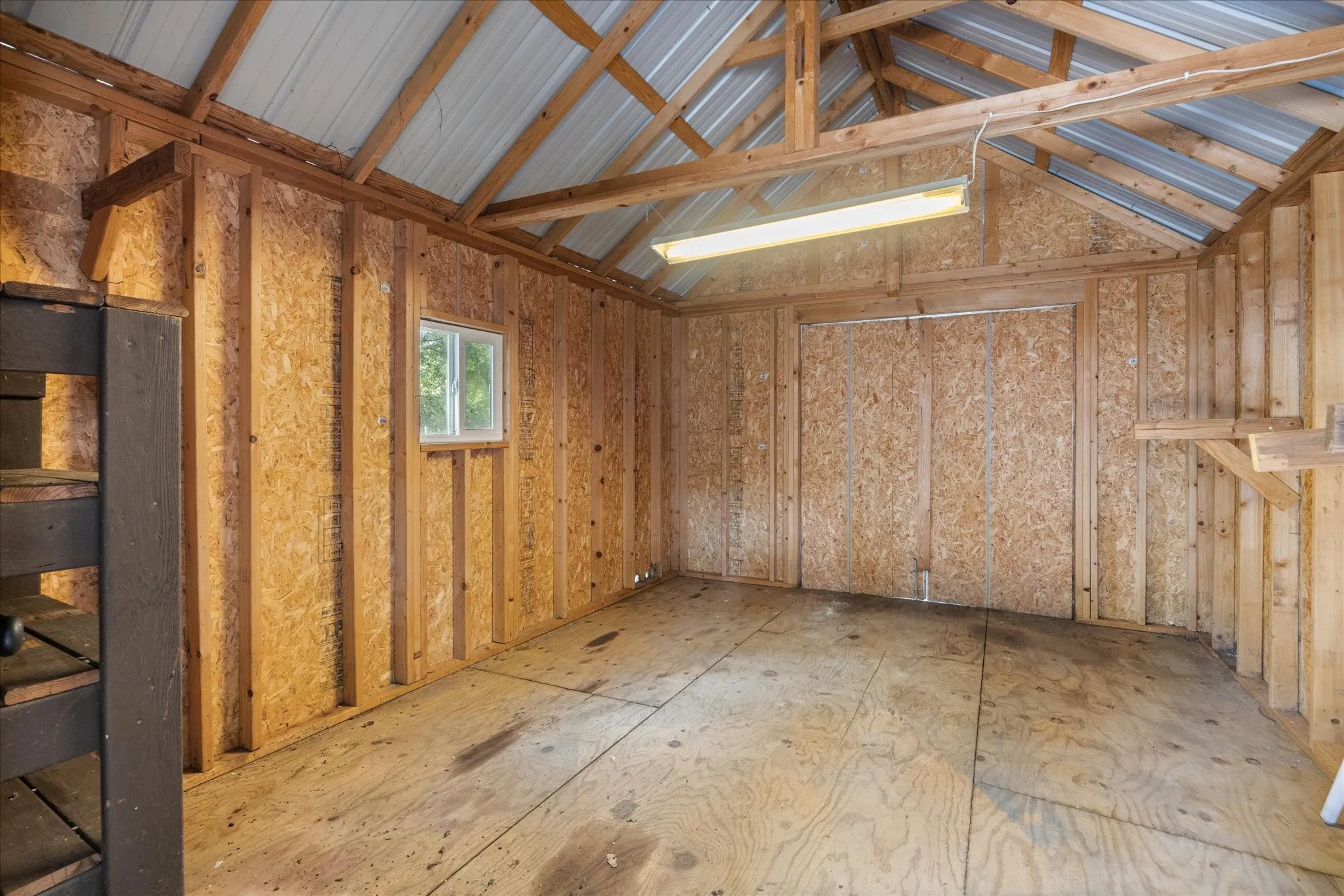 Interior storage space featuring exposed wood framing, wood-finish paneling, a gabled metal roof, and a fluorescent light fixture