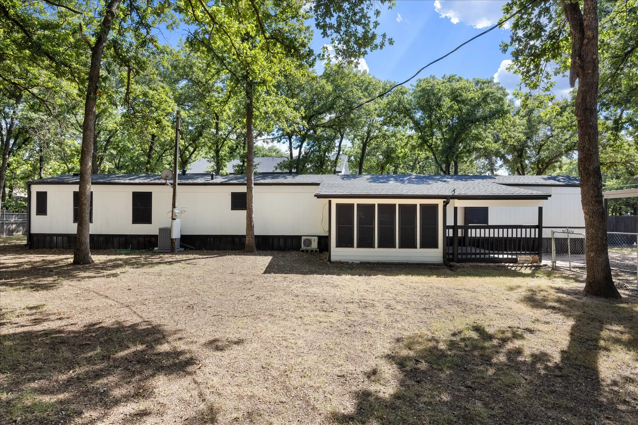 Expansive backyard featuring a screened-in porch with dark railing, mature trees, and a white siding exterior