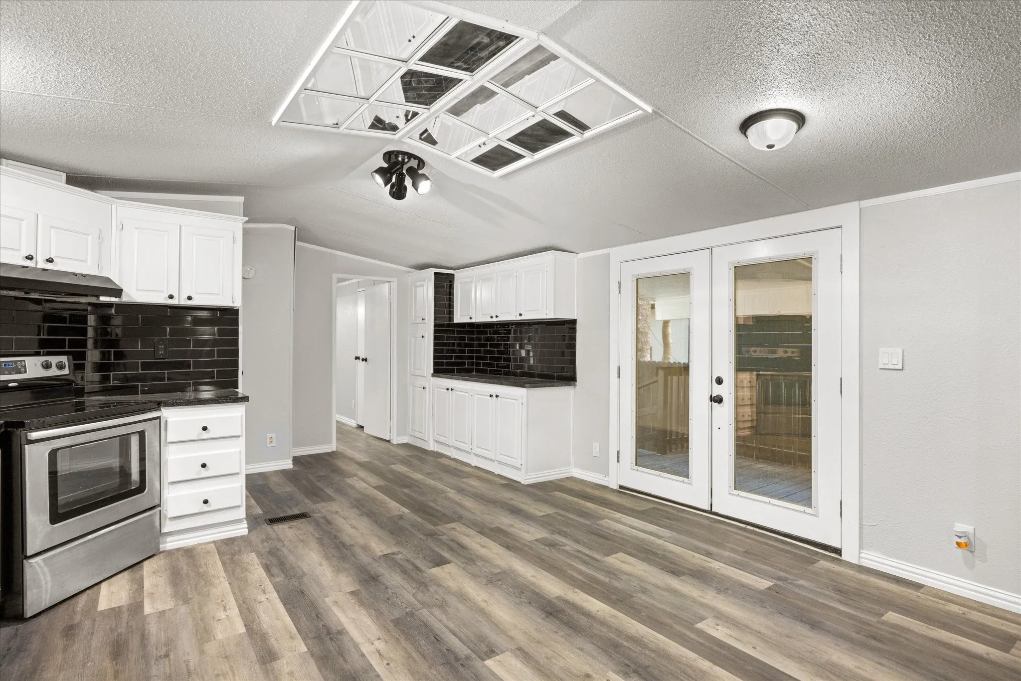 Contemporary kitchen featuring stainless steel appliances, crisp white cabinetry with black hardware, and a contrasting black subway tile backsplash