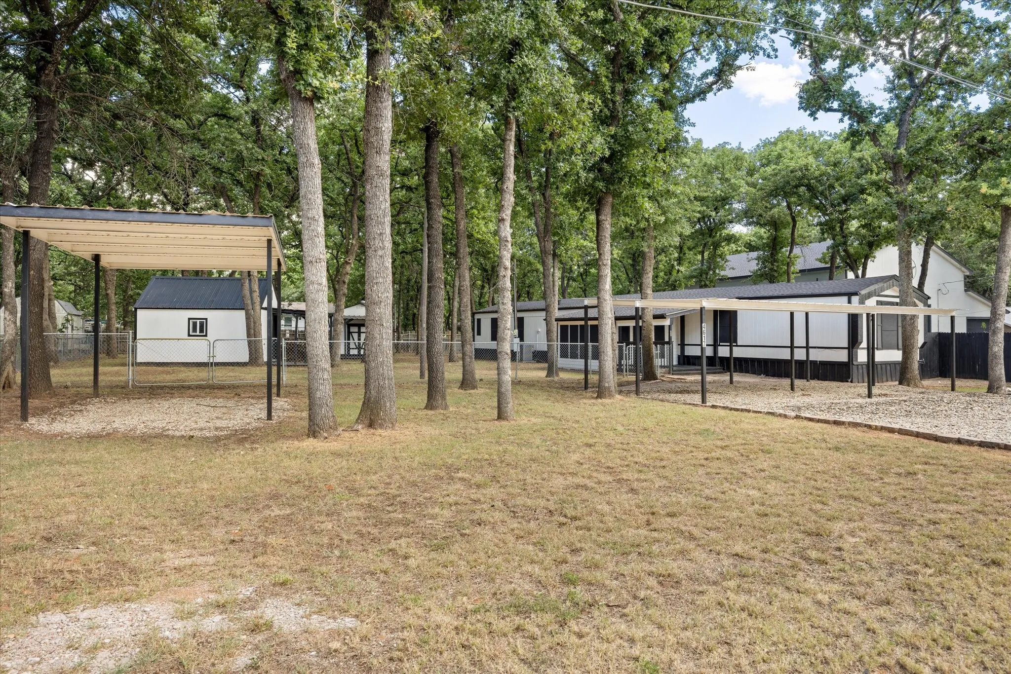 4617 Lyndi Ln
Granbury, TX  76049 Expansive property featuring multiple carports, a white exterior building with a dark roof, and a gravel surface