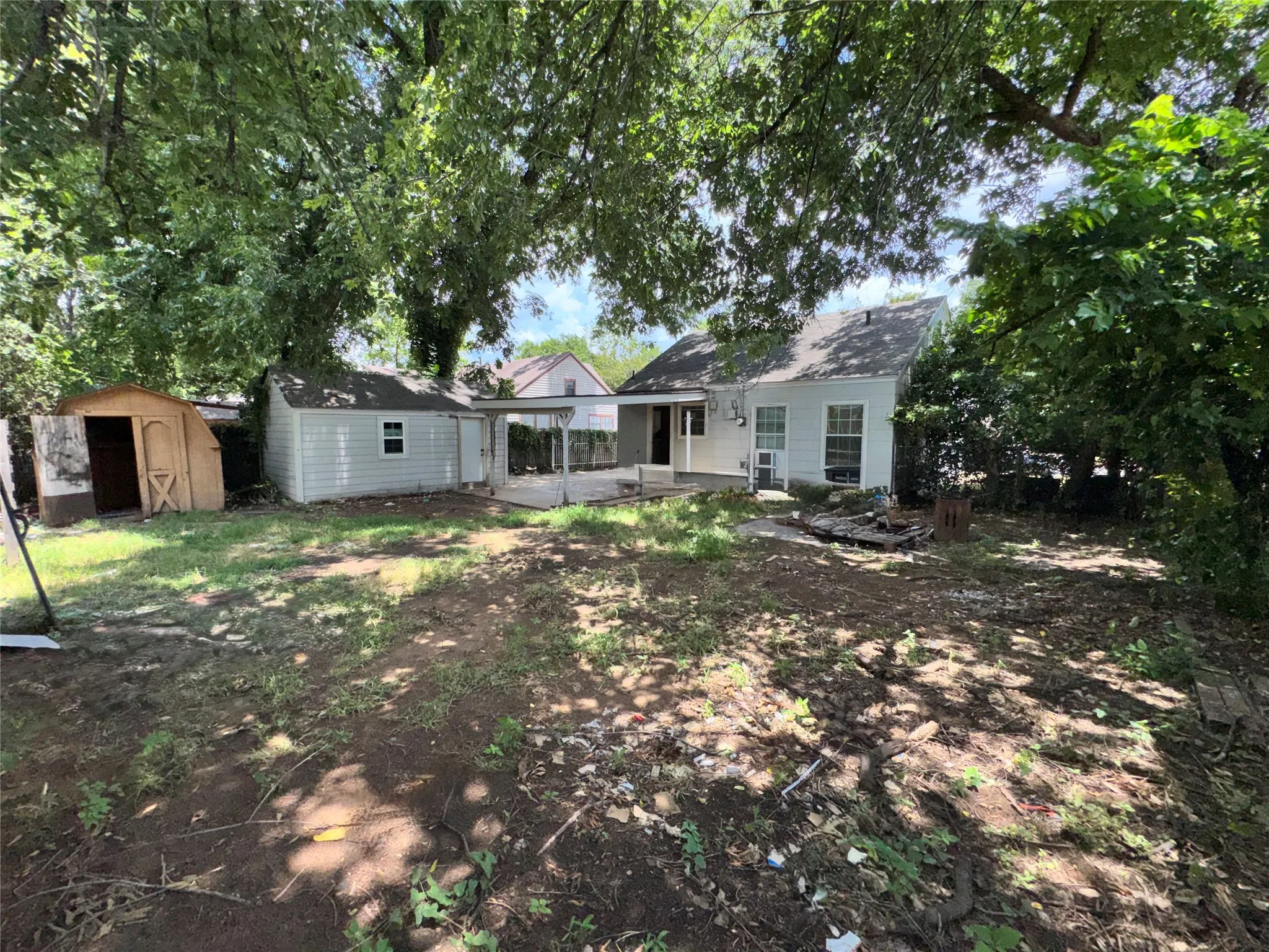 Expansive backyard featuring mature trees, a covered patio area, and a detached shed