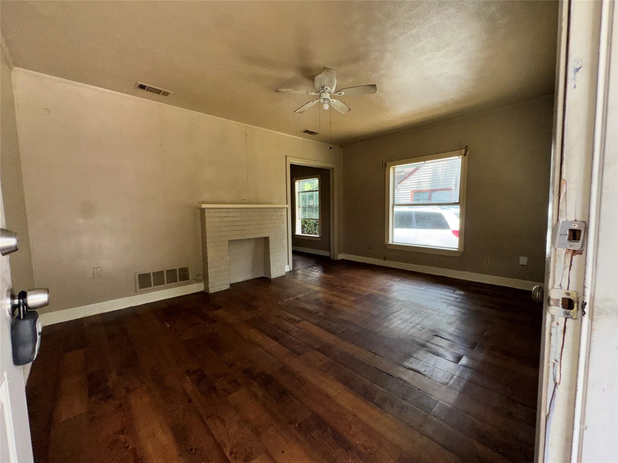 Living space featuring wood-finish flooring, a white brick fireplace, and a ceiling fan