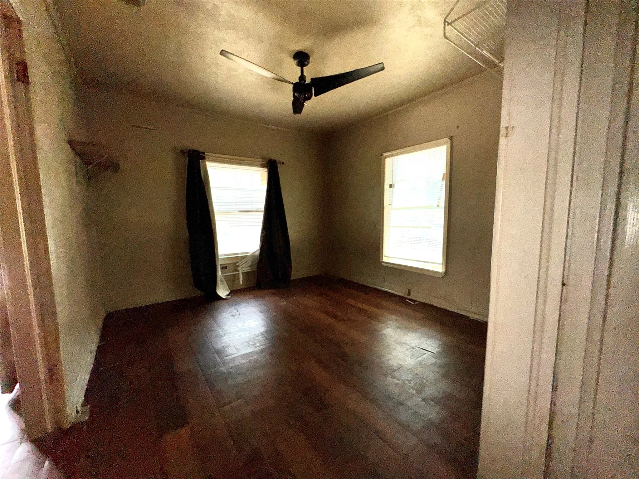 Room featuring wood-finish flooring, two window openings, and a ceiling fan with integrated lighting