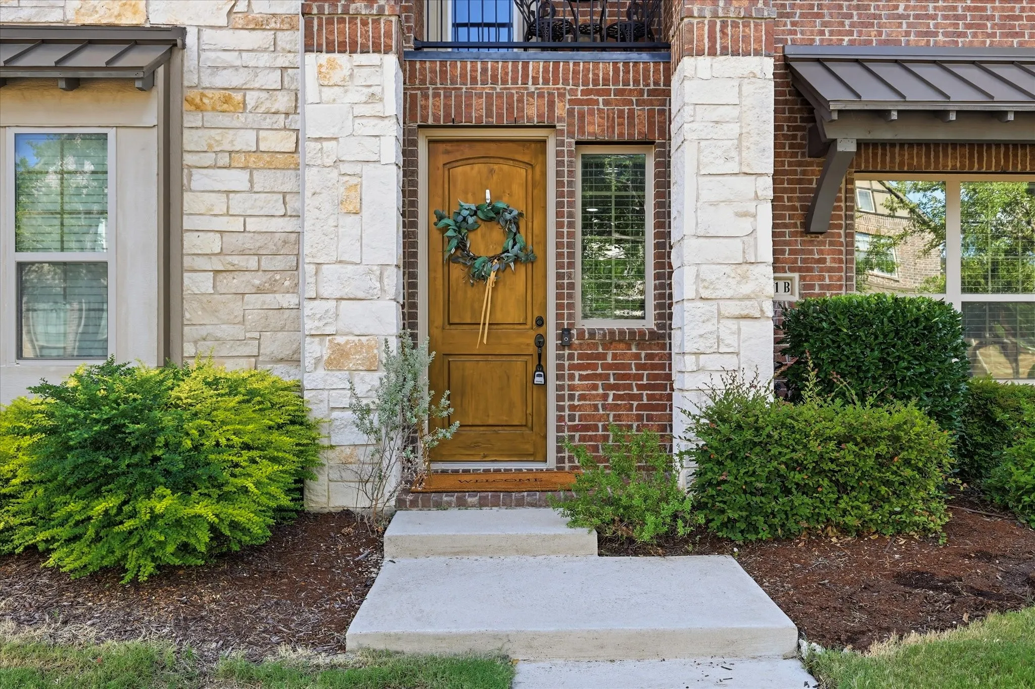 Exterior brick and stone facade featuring a natural wood-finish door, covered entryway, and mature landscaping