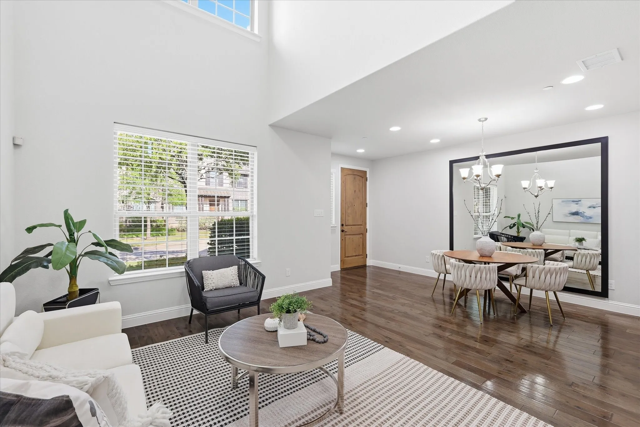 Open-concept living area featuring a two-story ceiling, large windows with operable blinds, and dark wood-finish flooring