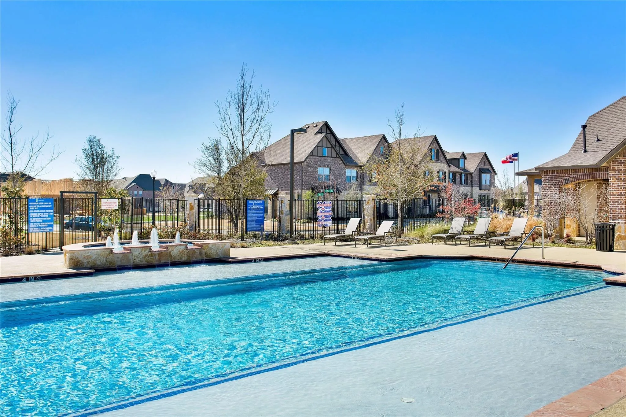 Outdoor swimming pool with integrated fountains, a surrounding concrete deck, and a fenced perimeter