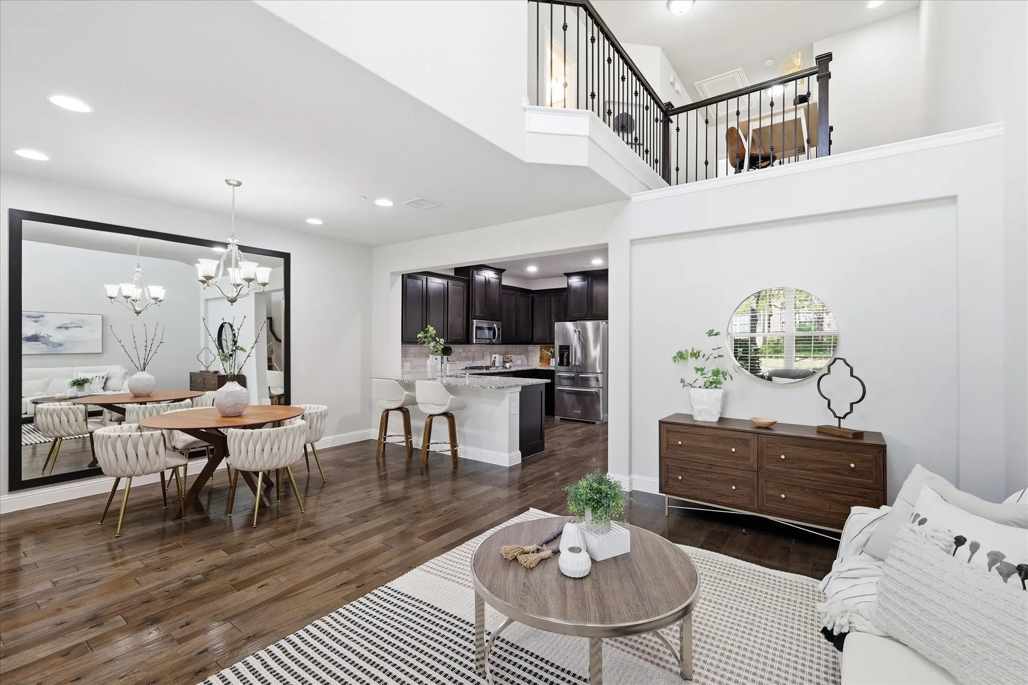 Open-concept living space featuring wood-finish flooring, recessed lighting, a modern chandelier, and a second-story overlook with wrought iron railing