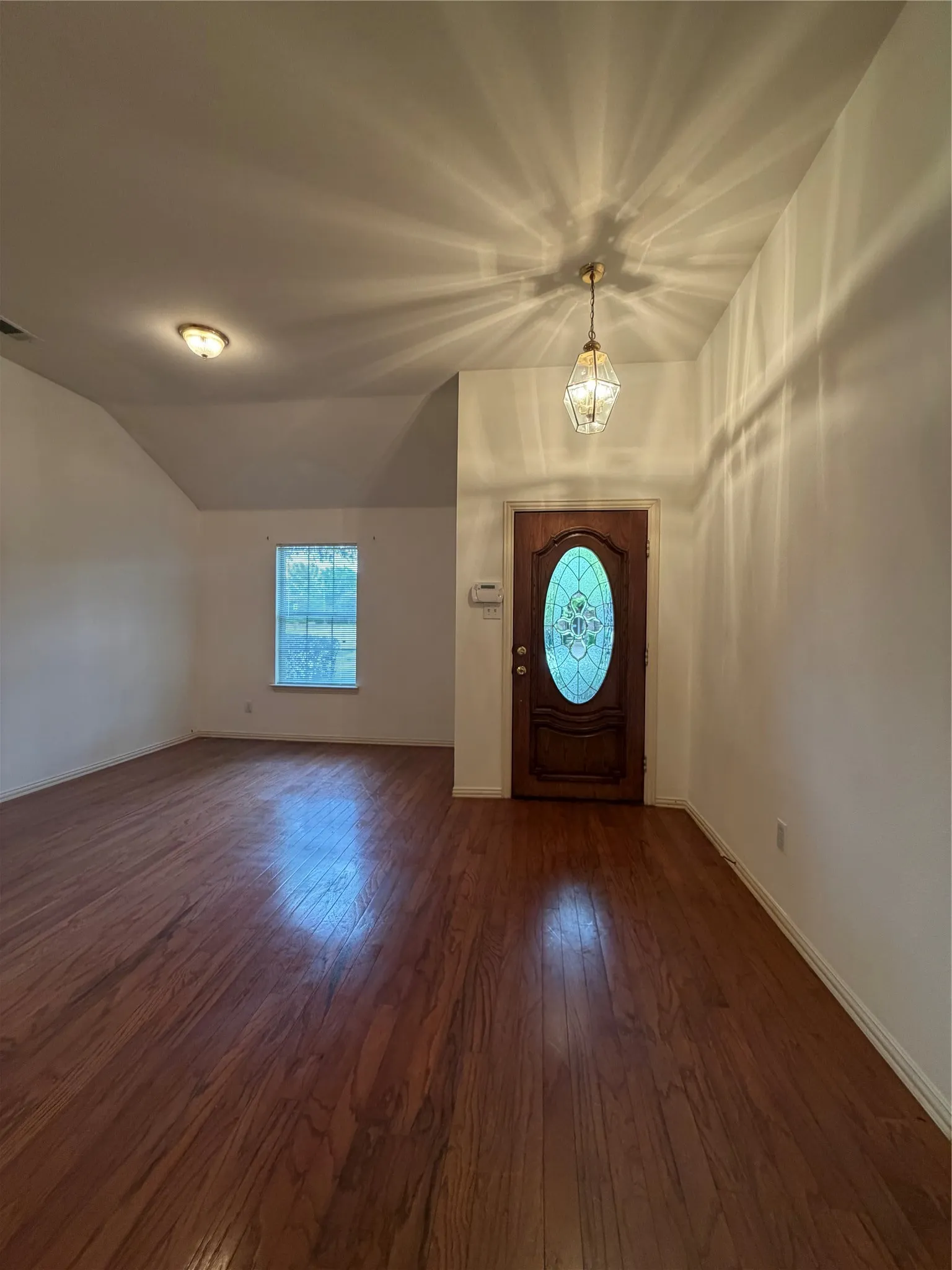 Entryway featuring a decorative wood-panel door with an oval stained-glass insert, wood-finish flooring, and a pendant light fixture
