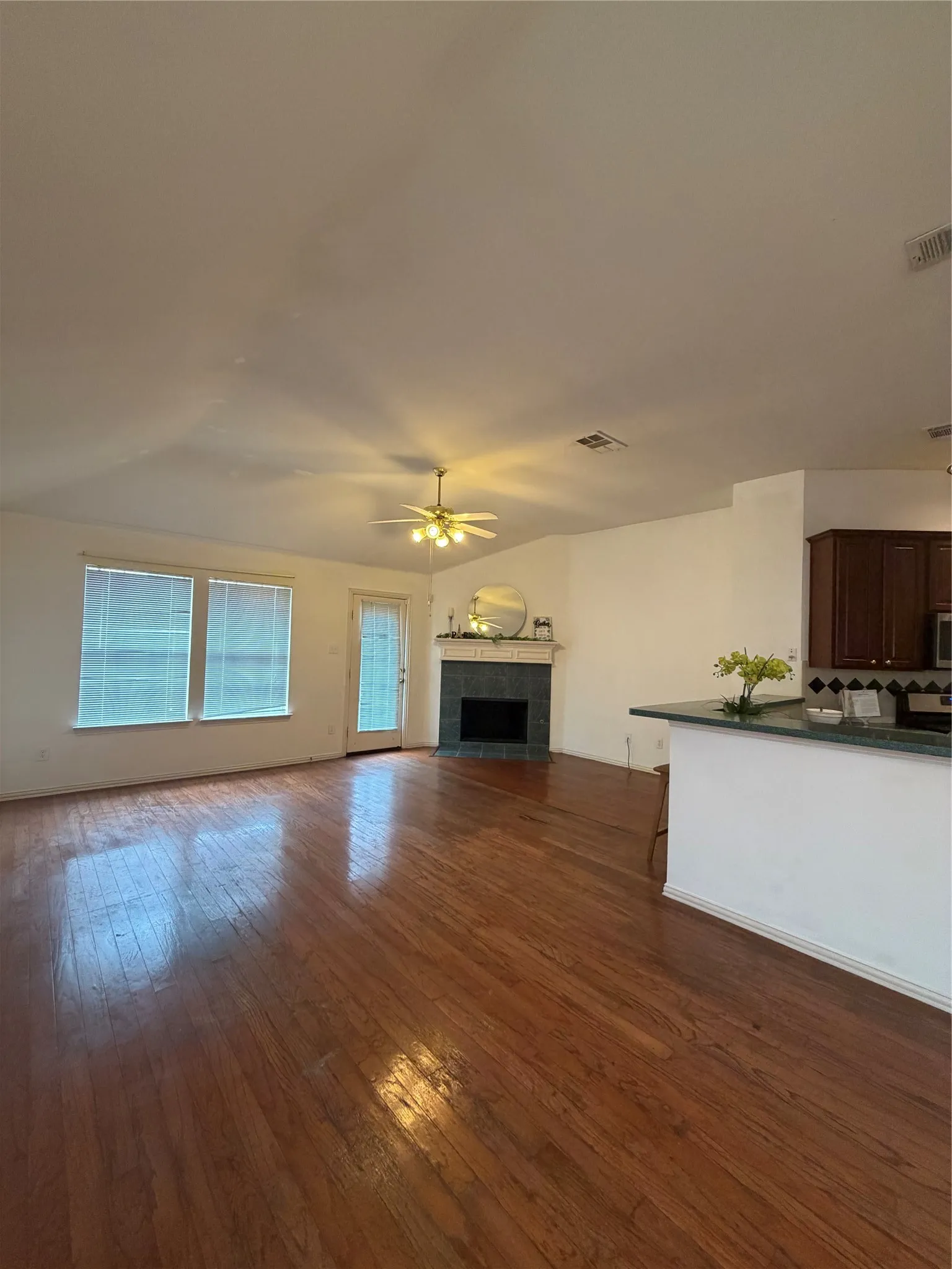 Spacious living area featuring rich wood-finish flooring, a vaulted ceiling with a ceiling fan, and multiple windows with blinds