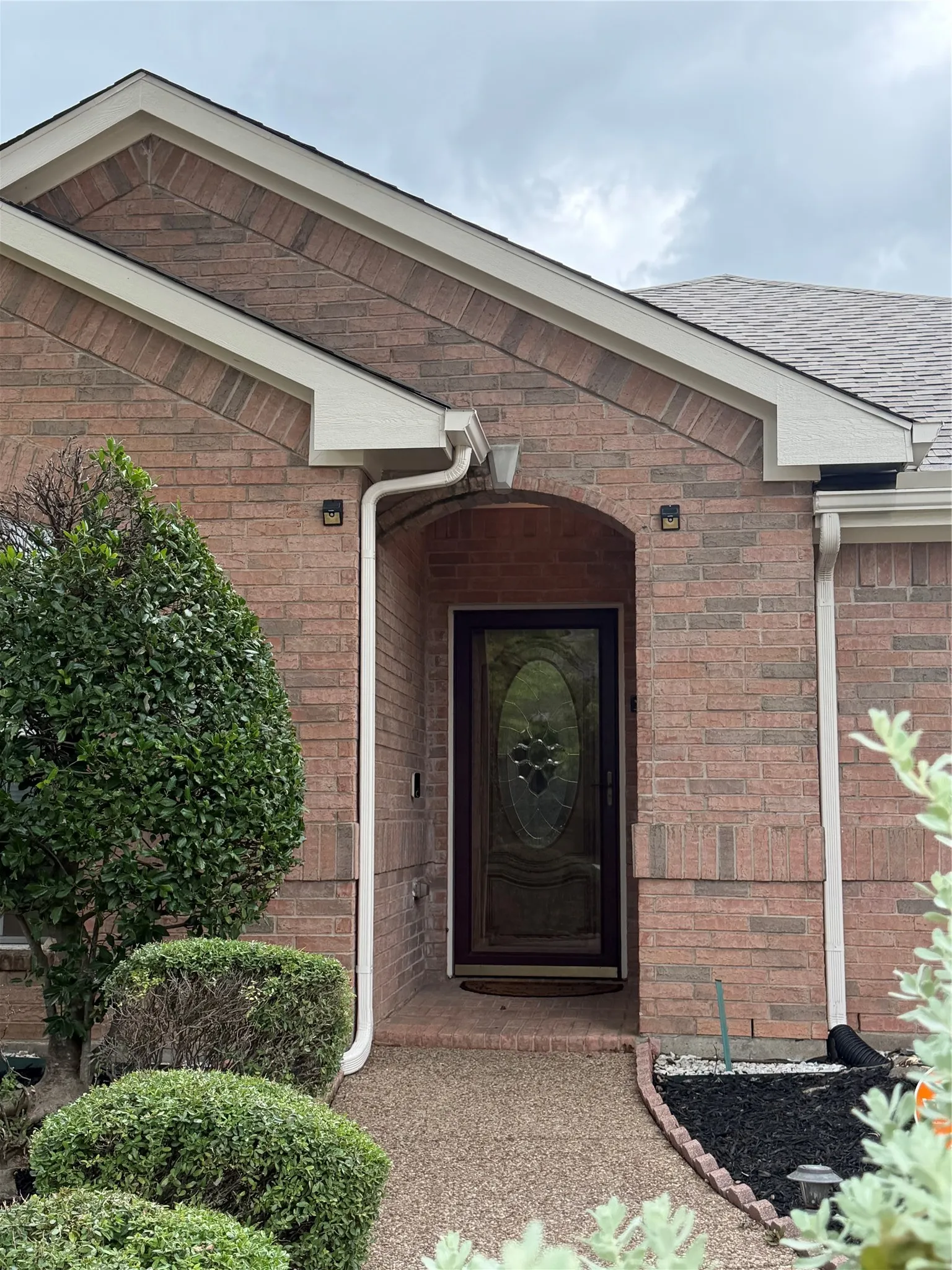Brick facade featuring an arched entryway with decorative glass door, flanked by exterior lighting fixtures