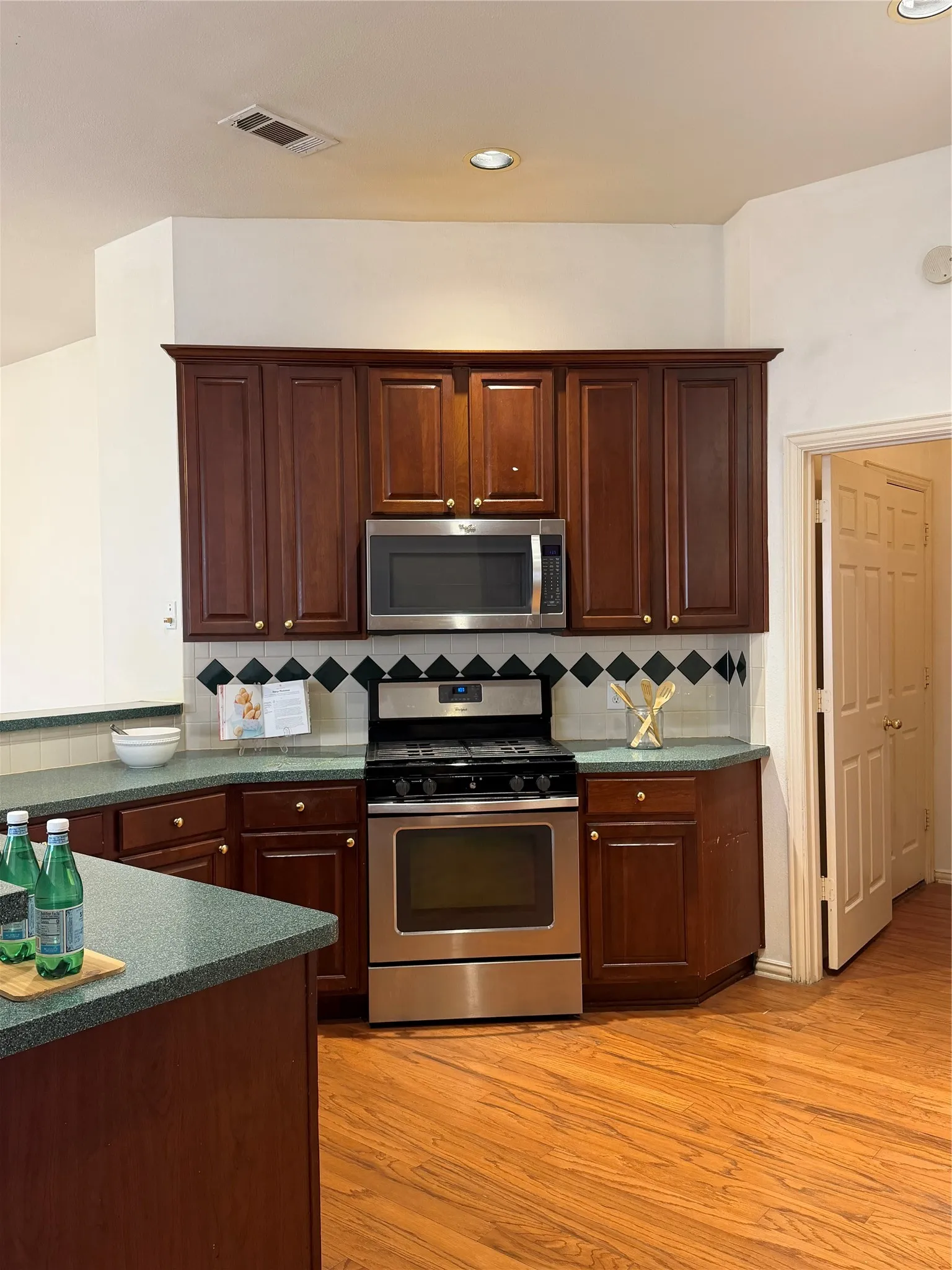 Kitchen featuring wood-finish flooring, dark wood cabinetry with brass hardware, and a stainless steel oven/range and microwave