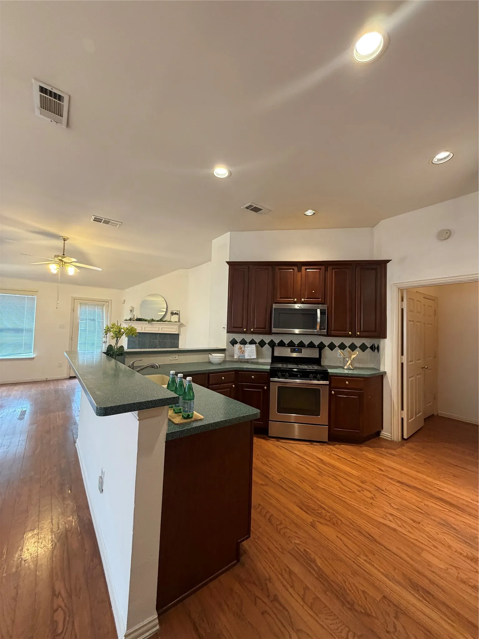 Open-concept kitchen featuring wood-finish flooring, dark wood cabinetry, stainless steel appliances, and a green countertop