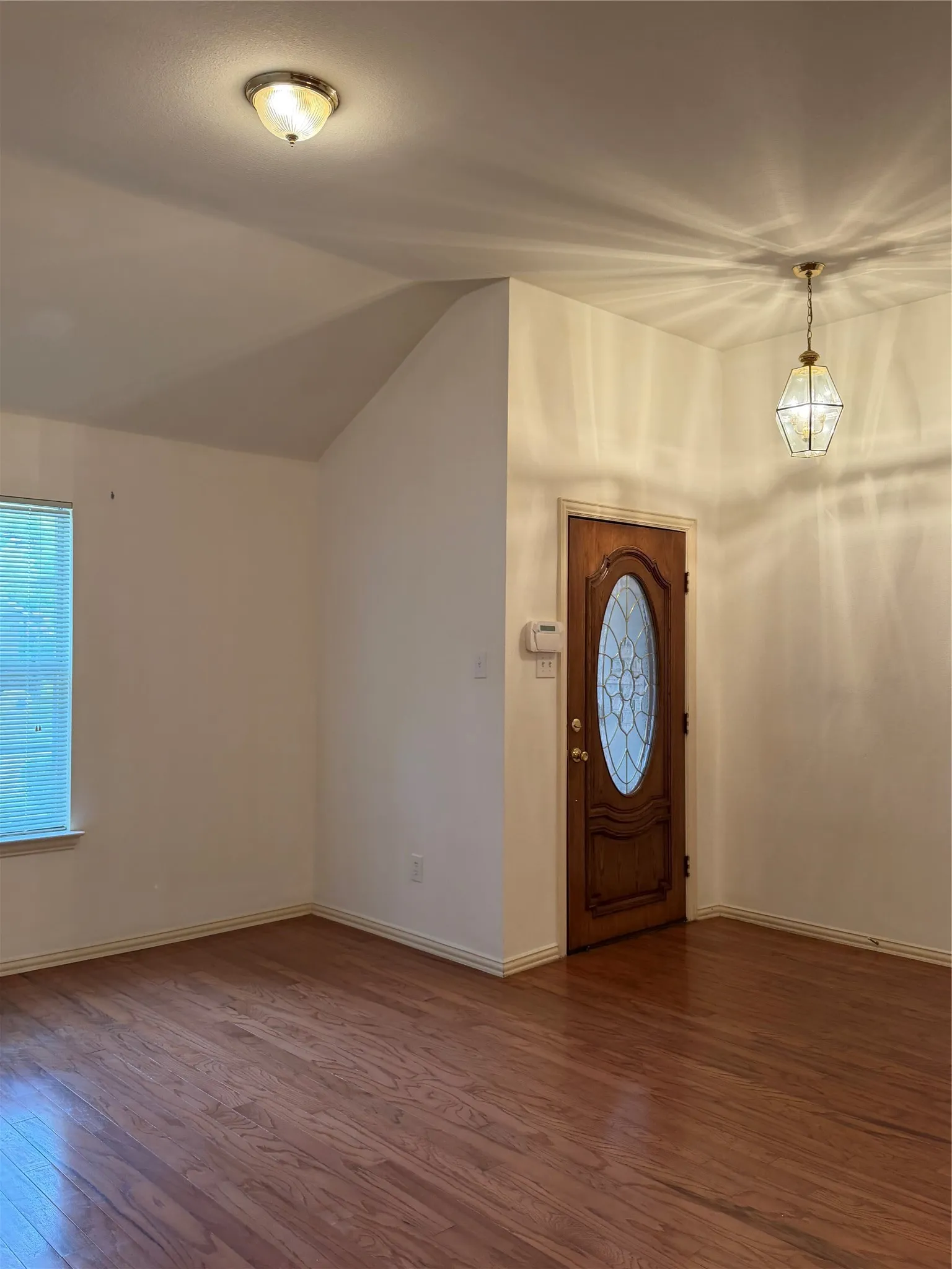 Entryway featuring rich wood-finish flooring, a decorative glass-paneled door, and a geometric pendant light fixture