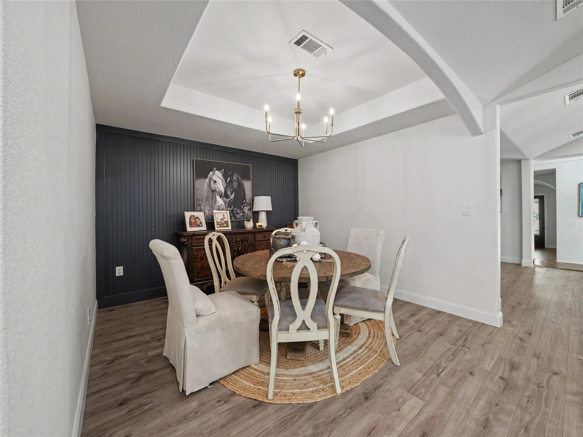 Dining area featuring a tray ceiling with a chandelier, wood-finish flooring, and a dark accent wall with vertical paneling