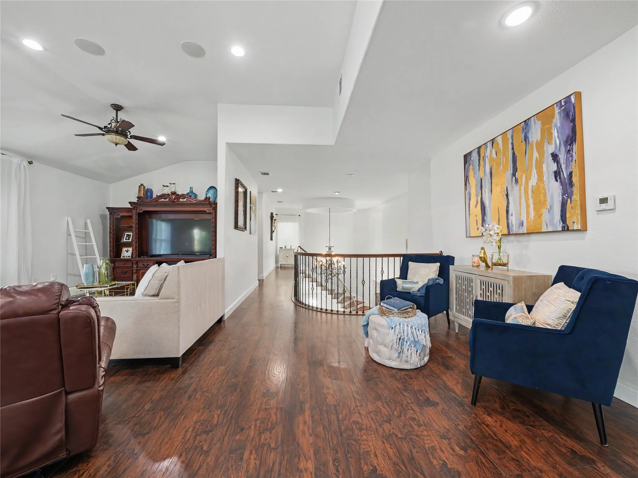 Spacious interior featuring rich wood-finish flooring, recessed lighting, a ceiling fan, and an open-concept design with a curved staircase railing