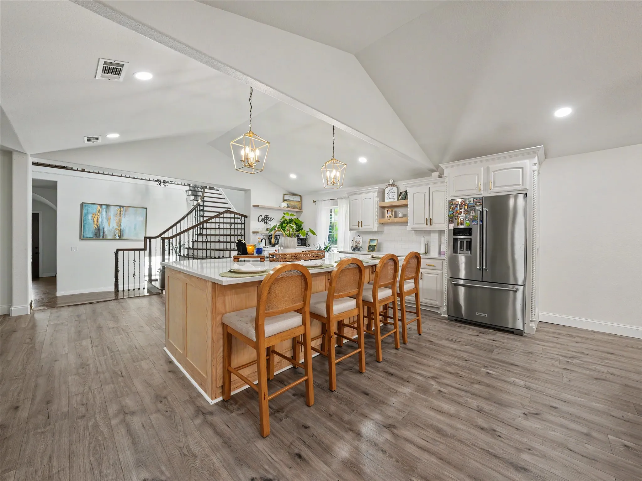 Open-concept kitchen featuring a large island with seating, stainless steel refrigerator, white cabinetry, vaulted ceiling, and wood-finish flooring
