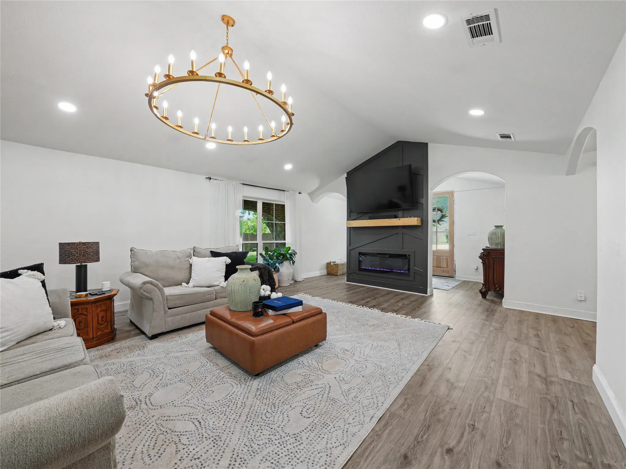 Spacious living area featuring wood-finish flooring, a modern electric fireplace with a wood mantel, and multiple recessed lights