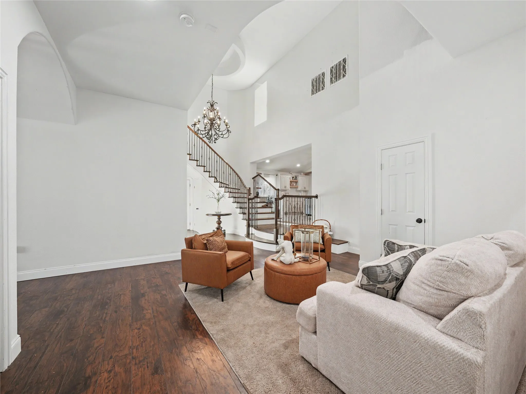Two-story entry featuring dark wood-finish flooring, a grand staircase with wrought iron balusters, a decorative chandelier, and vaulted ceilings