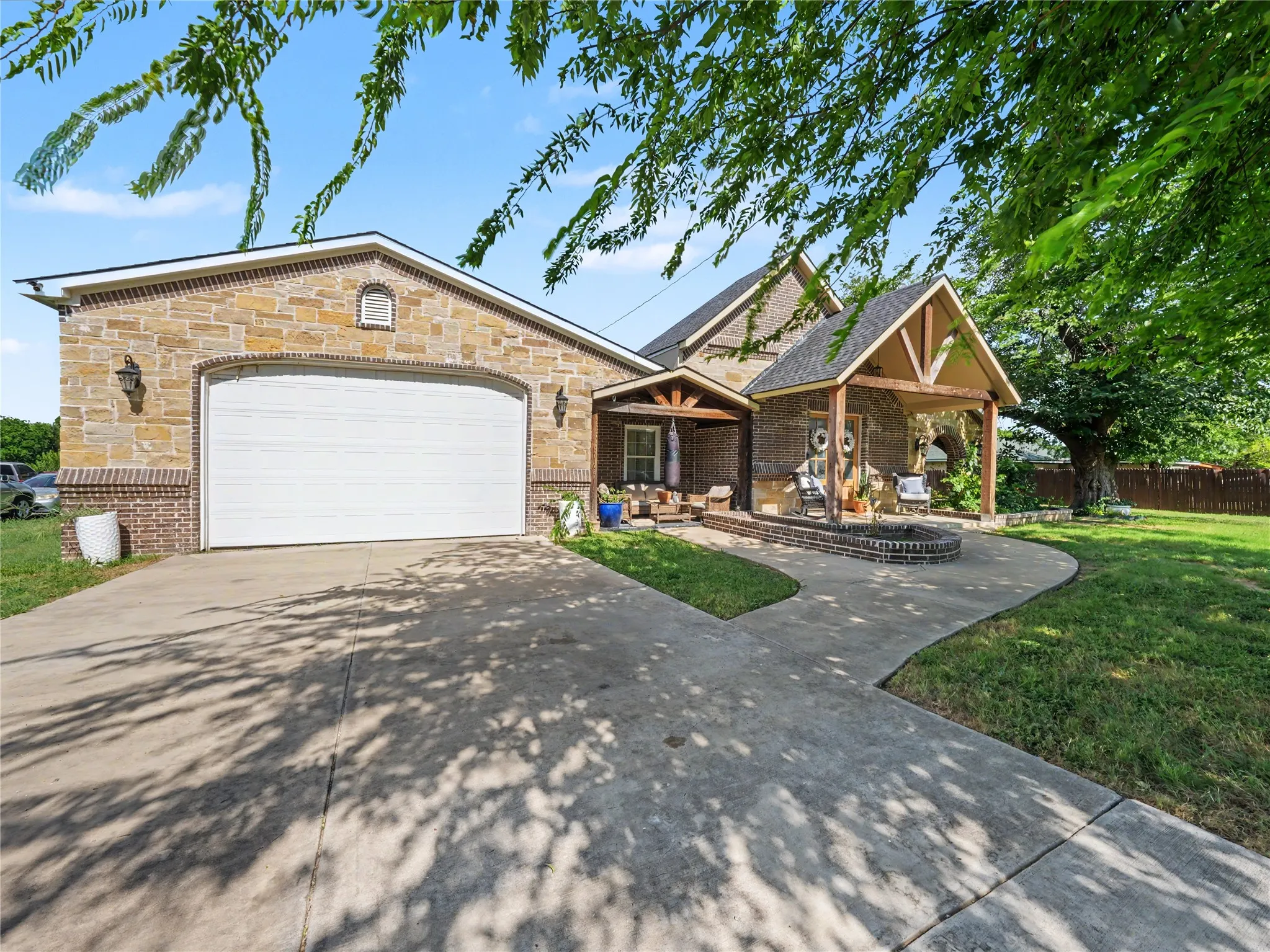 Stone and brick exterior featuring a covered entry porch with timber accents, a second covered porch, a concrete driveway, and an attached garage with an arched opening
