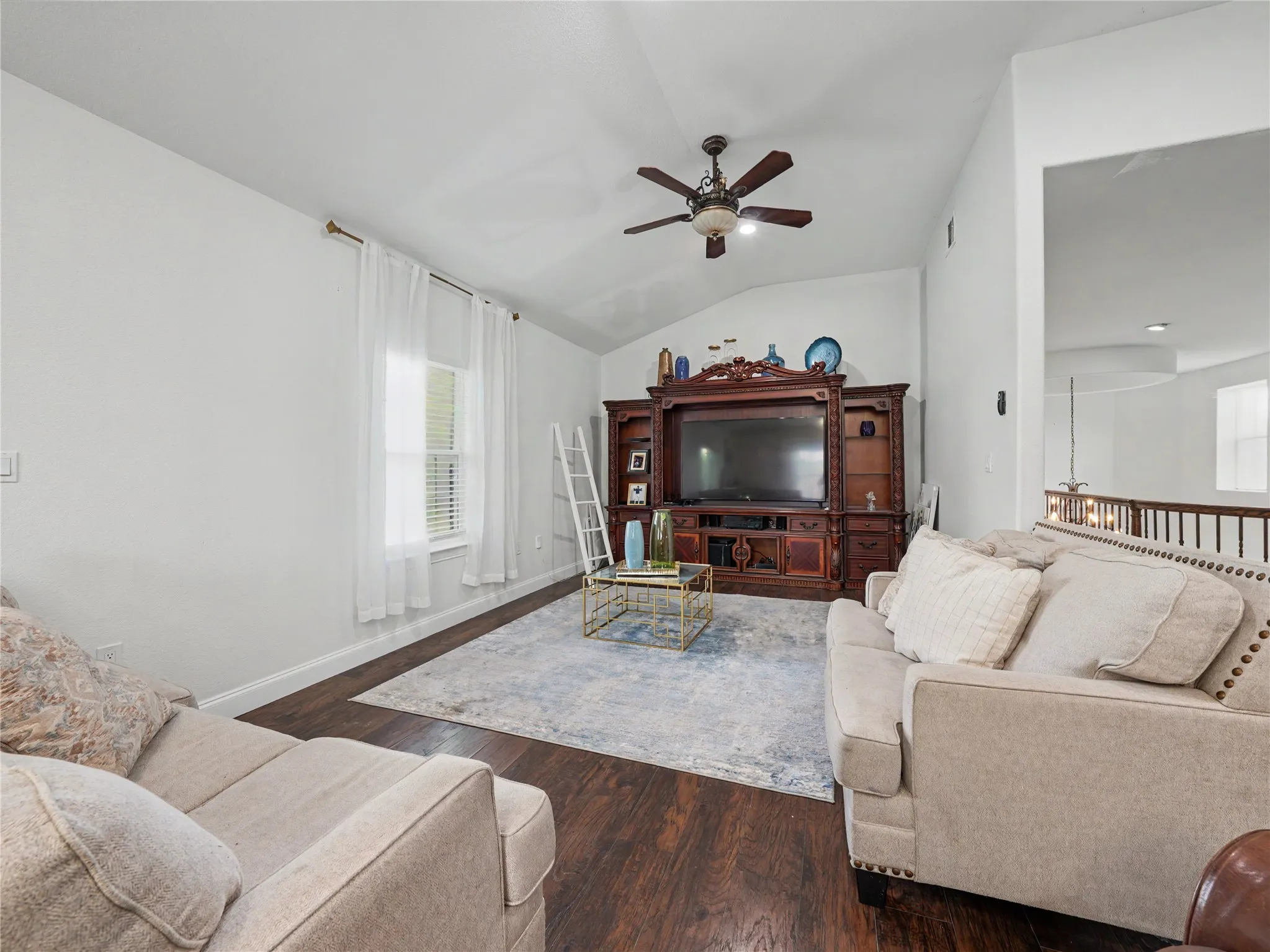 Living area with wood-finish flooring, vaulted ceiling, and a ceiling fan