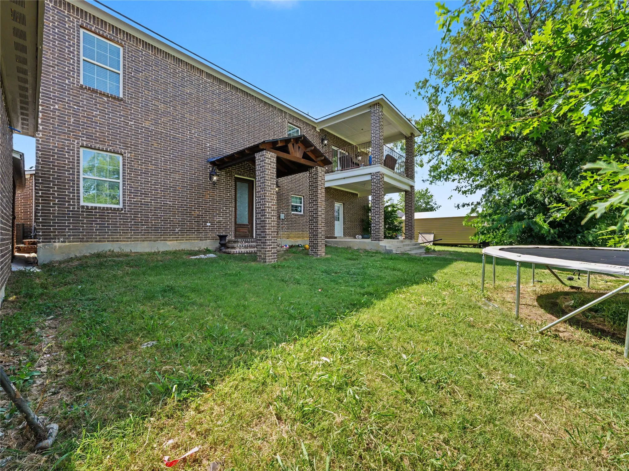 Brick exterior featuring a covered porch with exposed wood beams and a second-story balcony