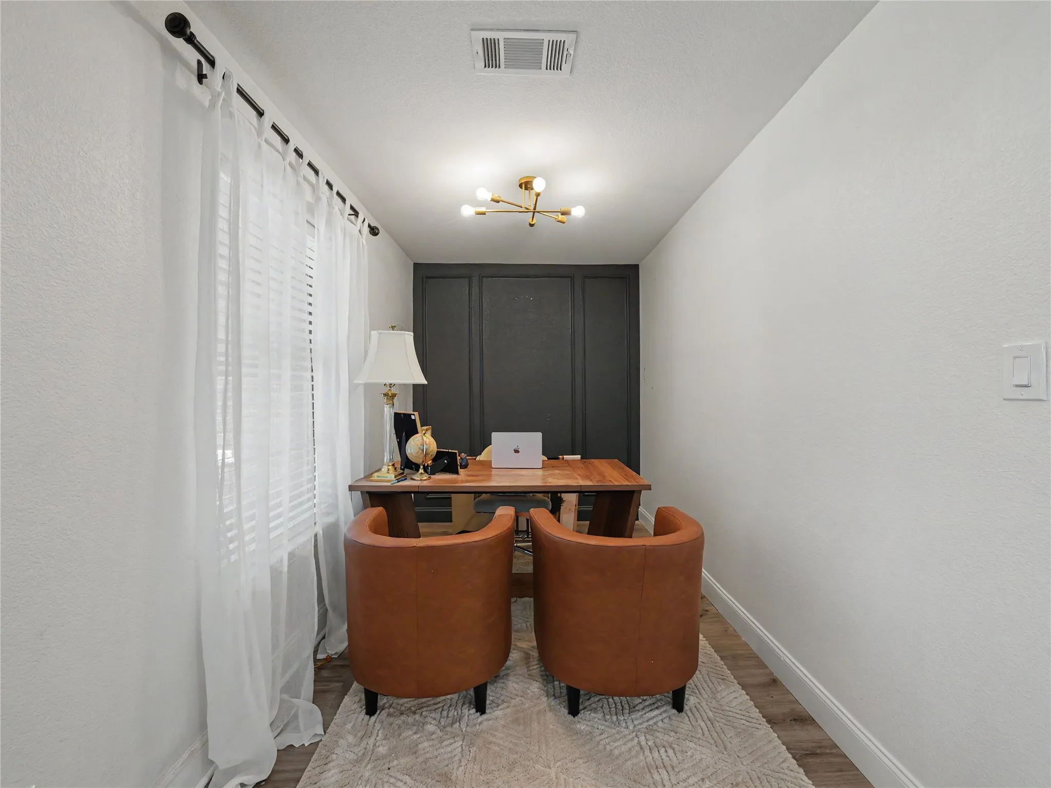 Dedicated interior space featuring a dark paneled accent wall, wood-finish flooring, and crisp white baseboards